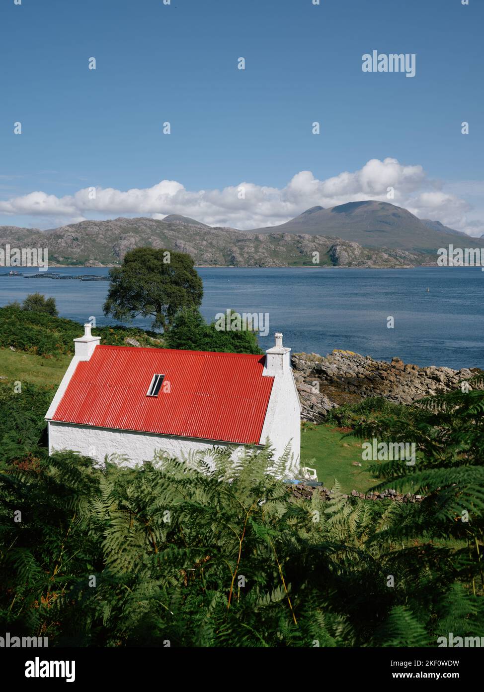 A red roofed white washed croft cottage overlooking Loch Shieldaig and the Torridon mountains landscape in Wester Ross, Scotland UK Stock Photo