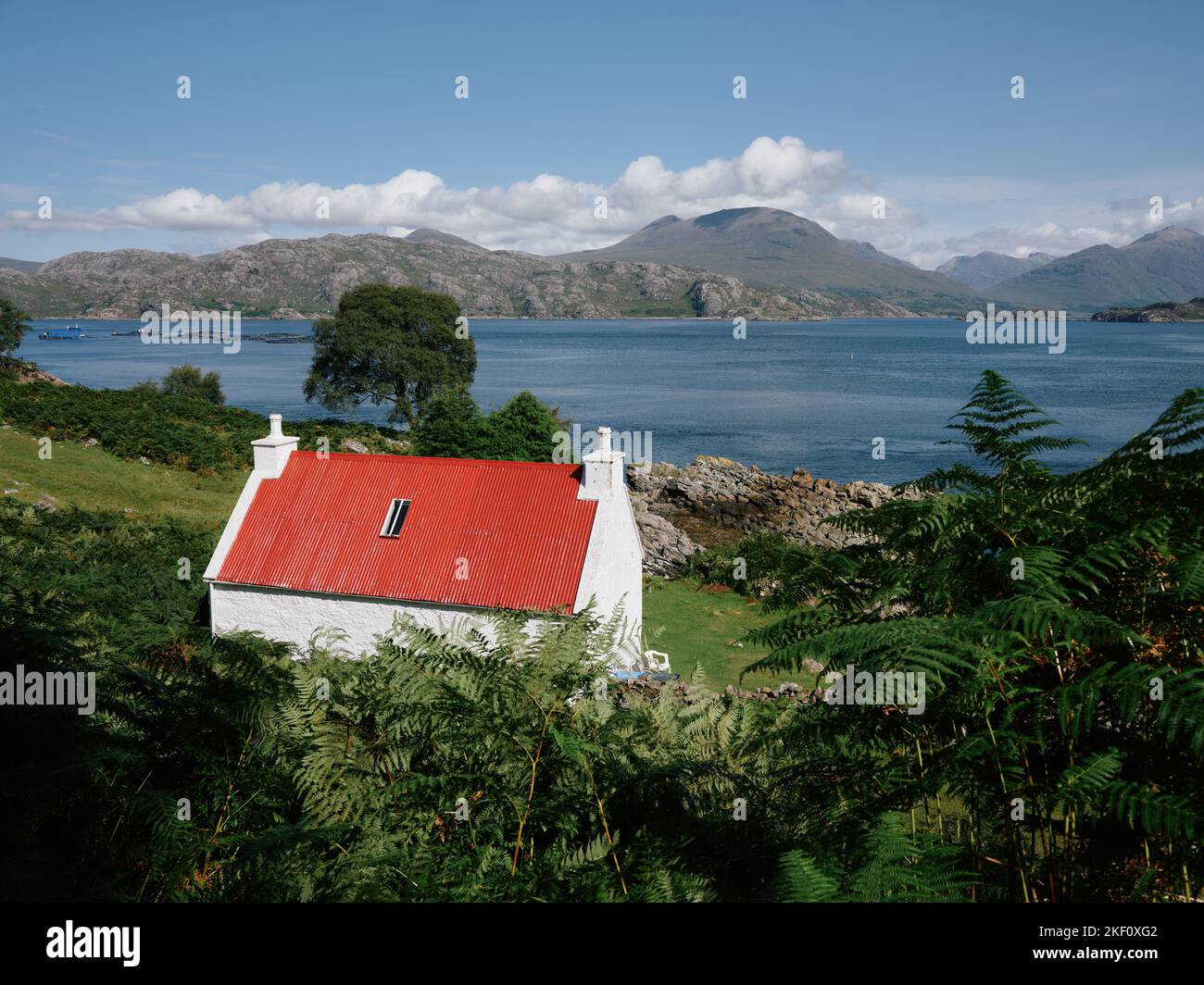 A red roofed white washed croft cottage overlooking Loch Shieldaig and the Torridon mountains landscape in Wester Ross, Scotland UK Stock Photo