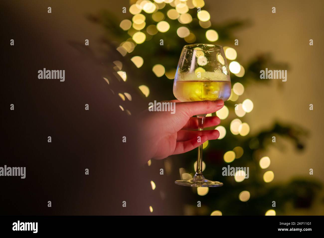 https://c8.alamy.com/comp/2KF11G1/hand-holding-glass-of-wine-blurry-christmas-lights-on-the-christmas-tree-in-the-background-pine-tree-decorated-with-shining-garland-person-holding-2KF11G1.jpg