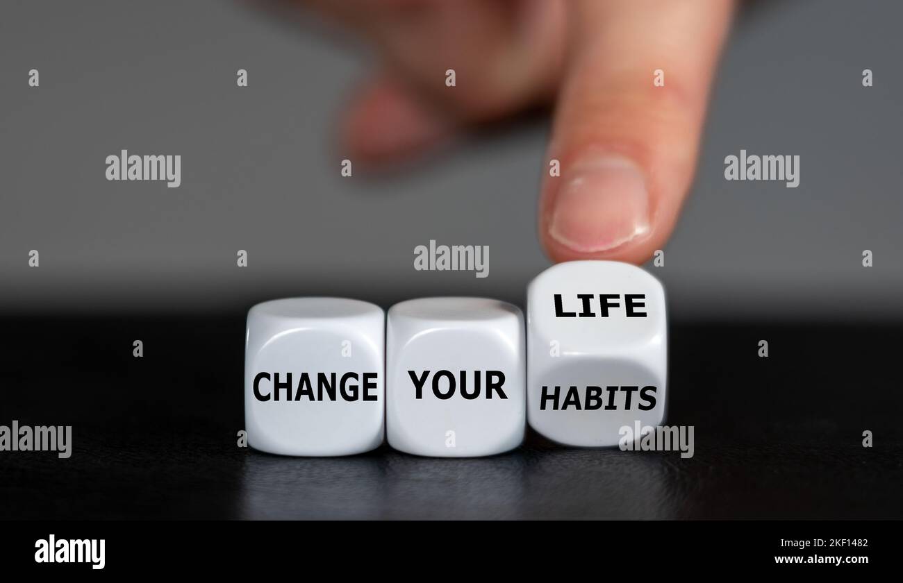 Hand turns dice and changes the slogan 'change your habits' to 'change your life'. Stock Photo