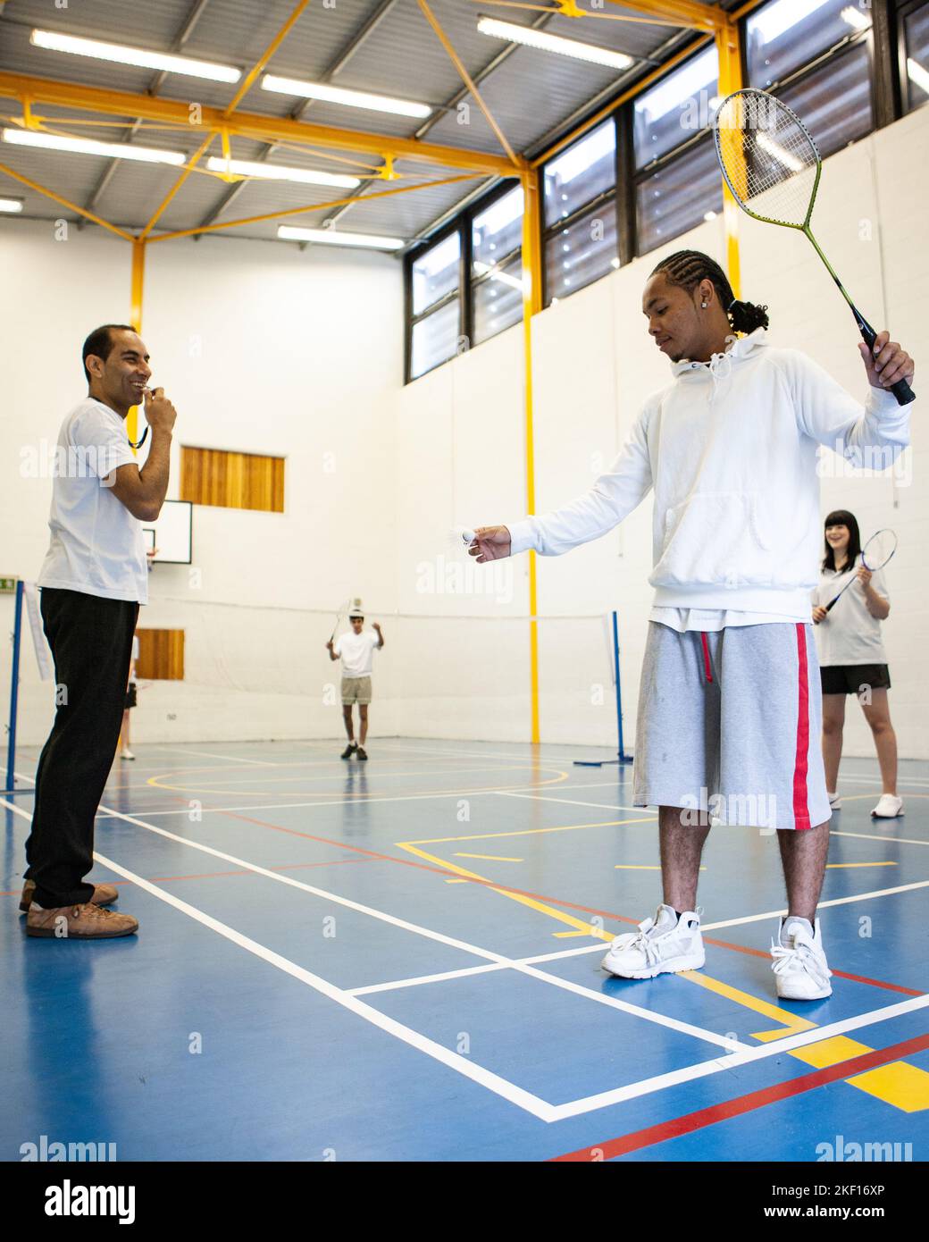 Sports Students: Badminton Mixed Doubles. Teenagers in their college gym under the supervision of their teacher. From a series of related images. Stock Photo