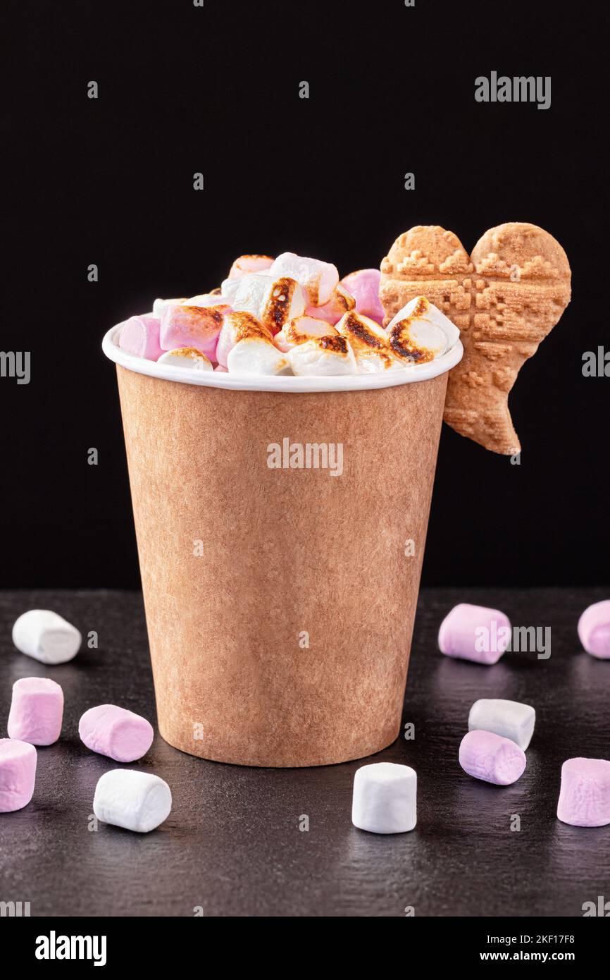 Paper cup with hot drink with marshmallows on dark background. Recycling and eco friendly