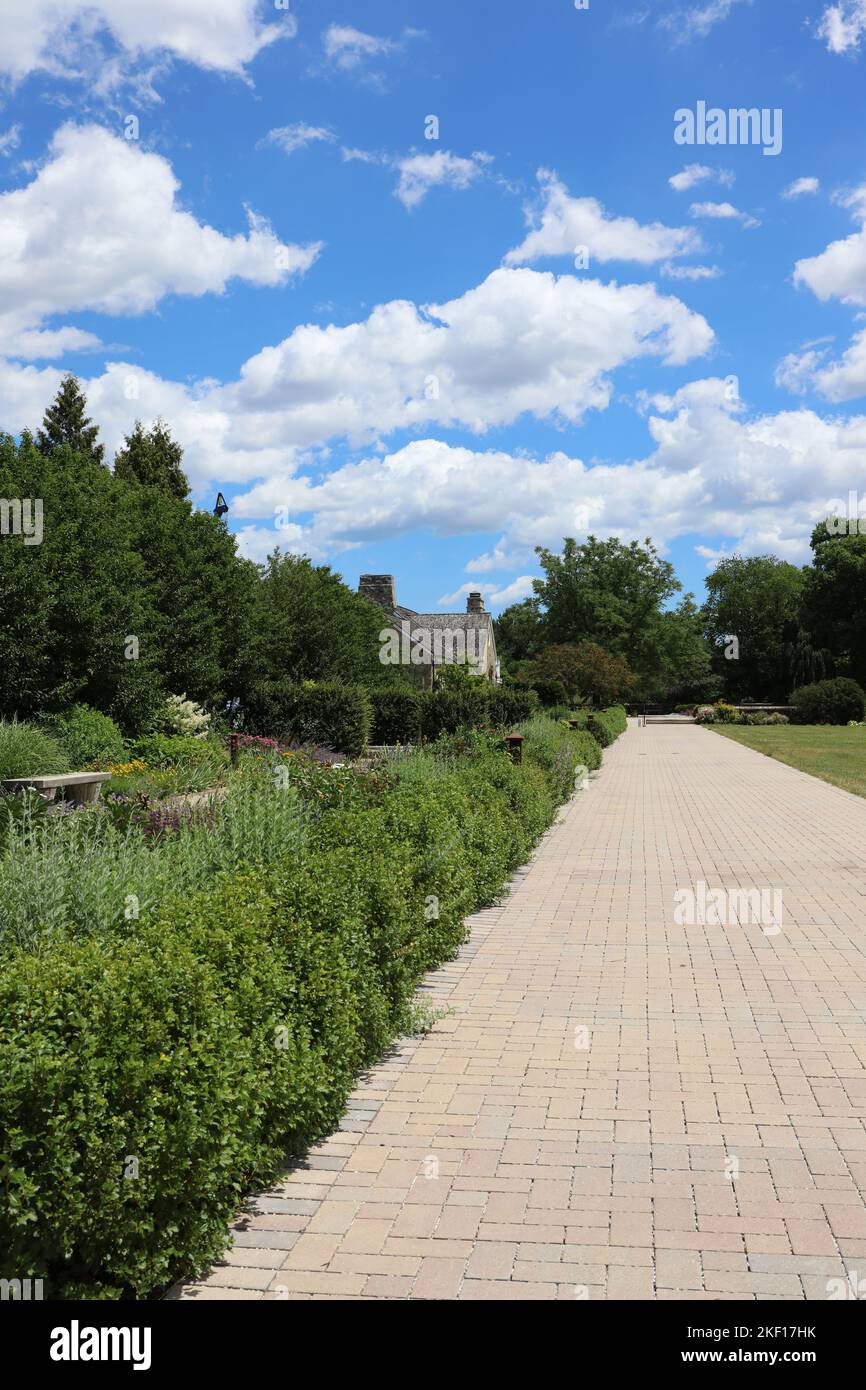 Rows of shrubbery and flowers lining a brick walkway leading to a cottage on a summer day in Boerner Botanical Gardens, Hales Corners, Wisconsin, USA Stock Photo