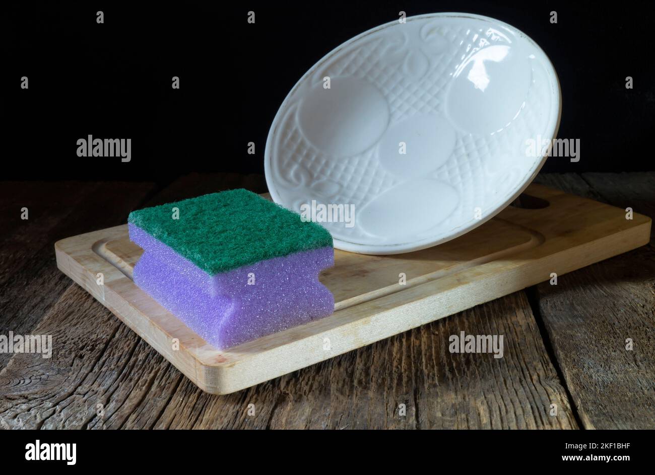 A dish washing sponge and a white plate on the table. Kitchen utensils on a black background Stock Photo