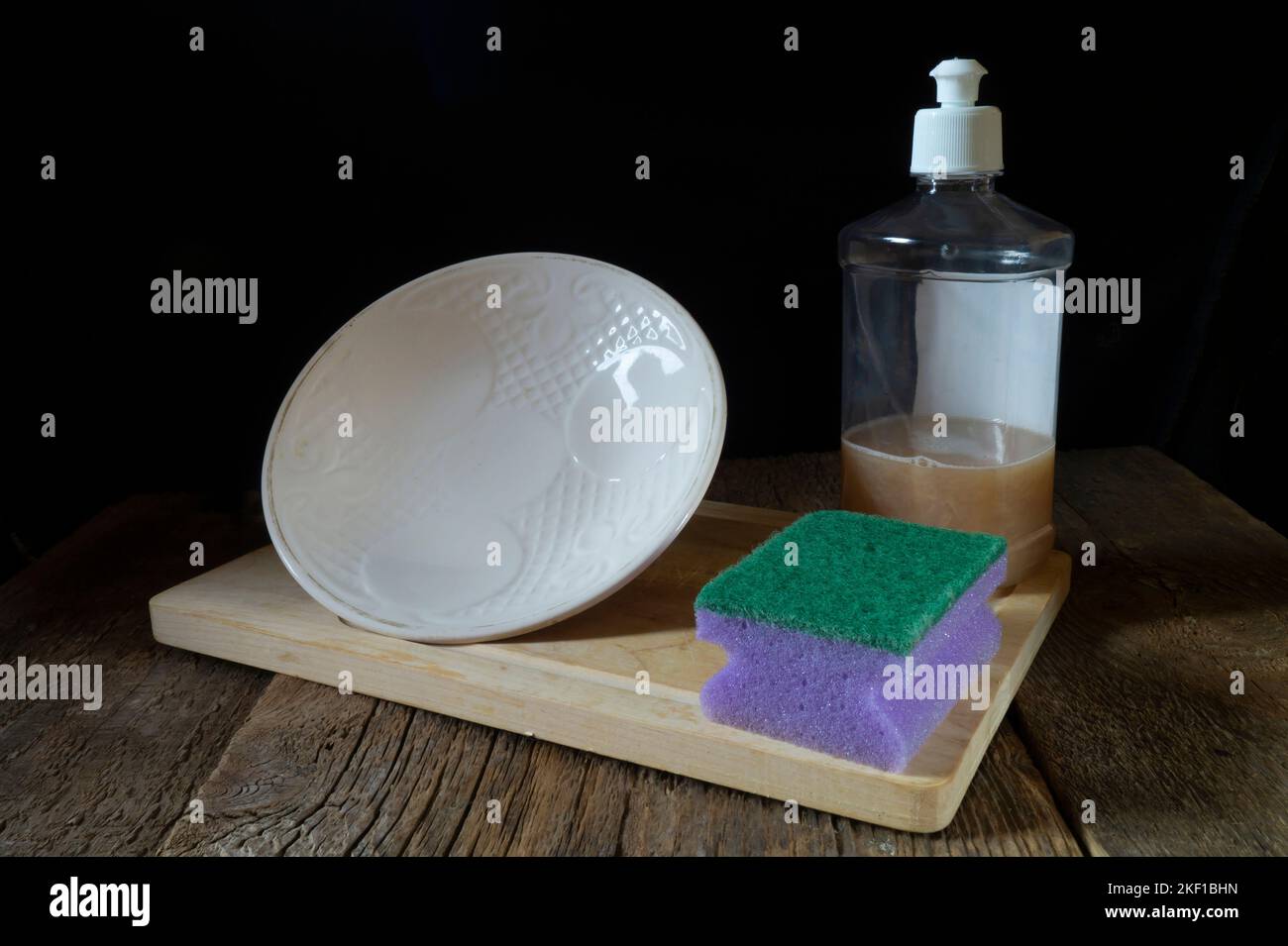 A dish washing sponge and a white plate on the table. Kitchen utensils on a black background Stock Photo