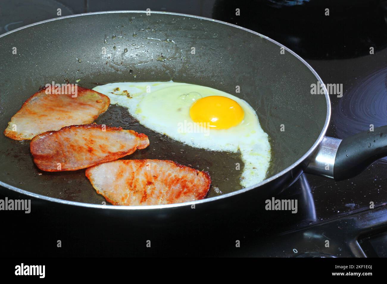 Egg and three rashers of bacon being fried in a frying pan for breakfast. Stock Photo