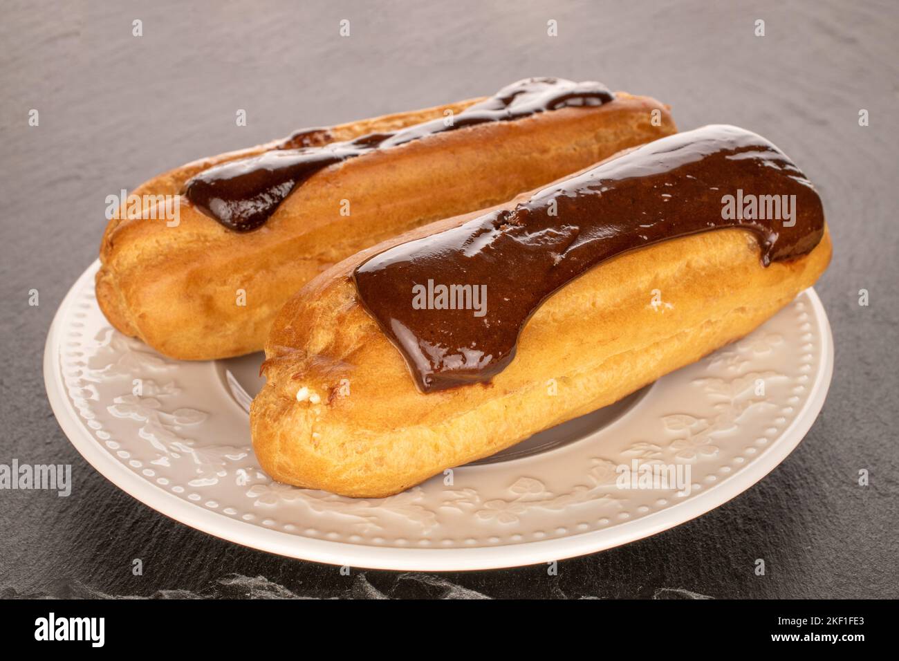 Two sweet eclairs with white plate on slate stone, macro. Stock Photo