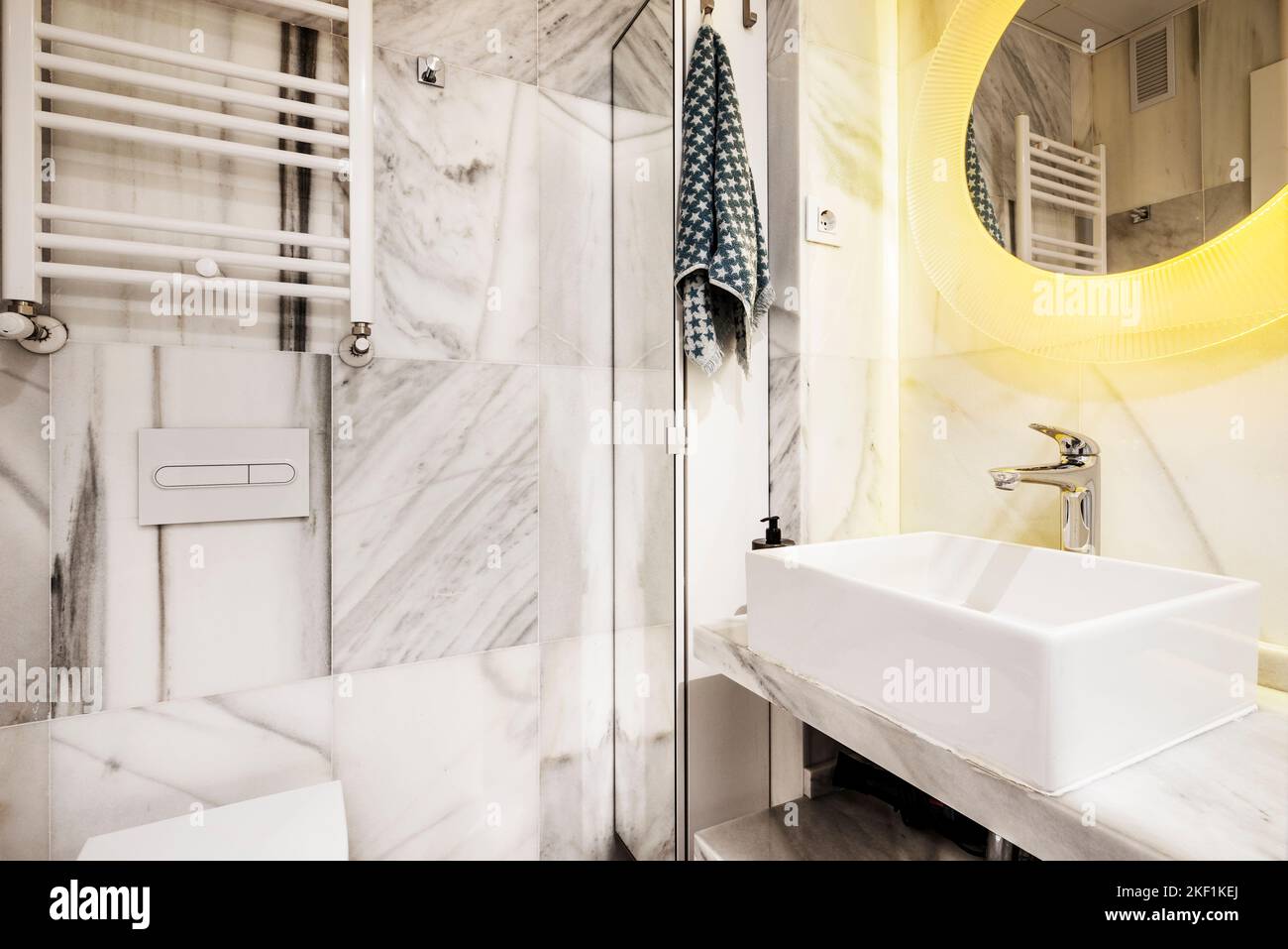 Bathroom tiled in white marble with gray veins, circular mirror and ...