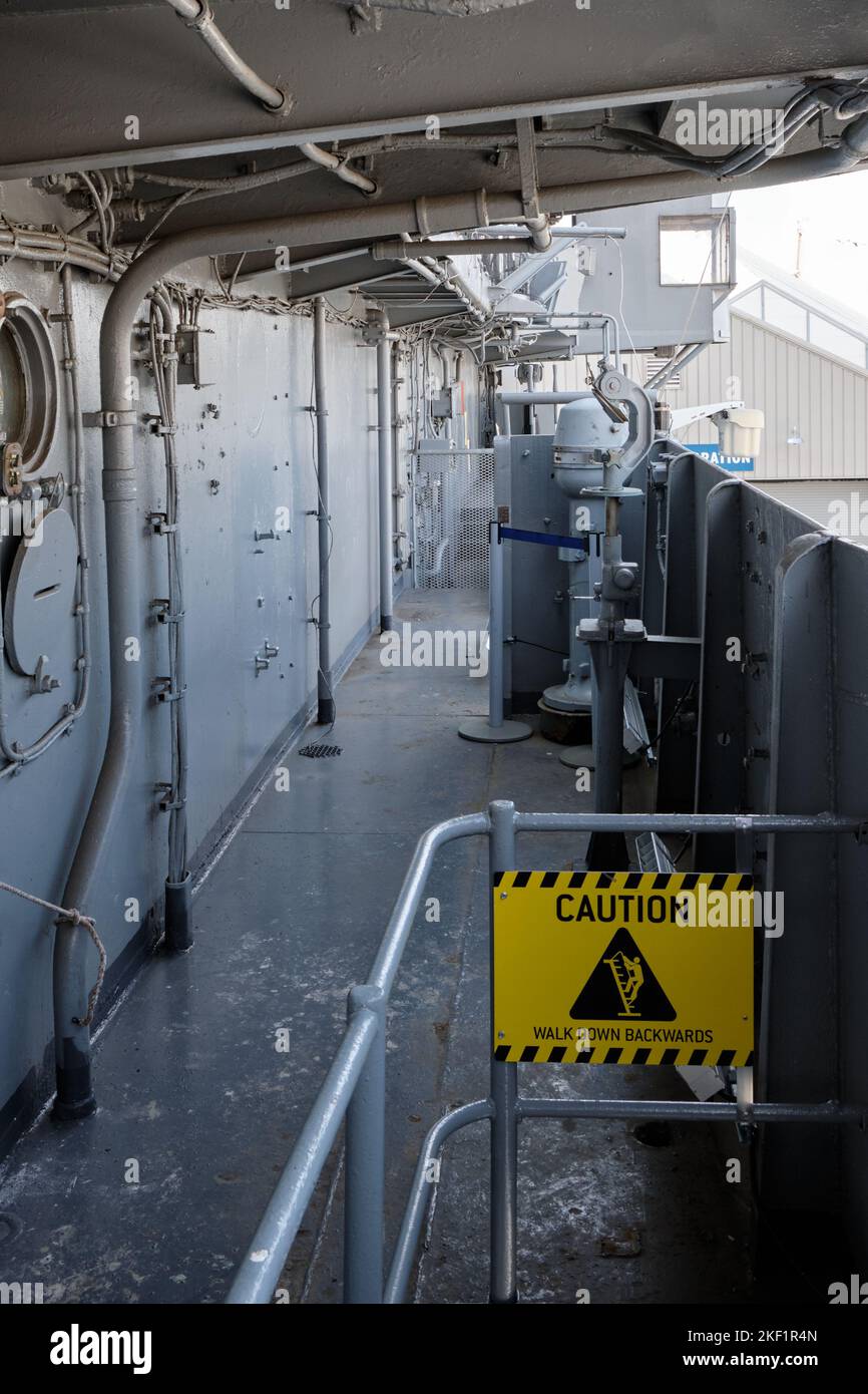Corridor of a US aircraft carrier warship, with a yellow caution sign. Intrepid Sea, Air & Space Museum Stock Photo