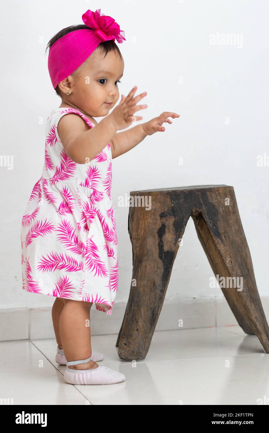 baby brunette learning to walk, letting go of the chair and raising her hands for balance Stock Photo