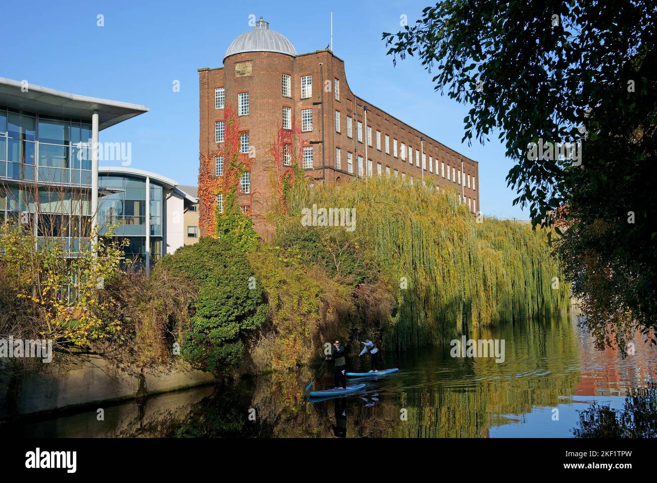 Stand-up paddleboarders on the River Wensum in Whitefriars, Norwich, beside historic St James Mill, home of Jarrolds Printers. Stock Photo
