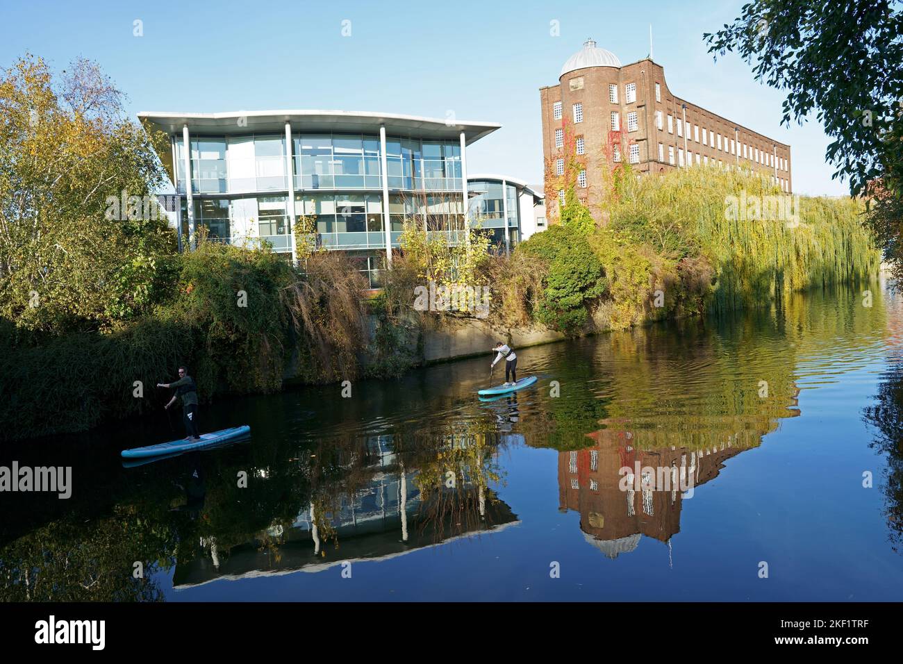 Stand-up paddleboarders on the River Wensum in Whitefriars, Norwich, beside historic St James Mill, home of Jarrolds Printers. Stock Photo