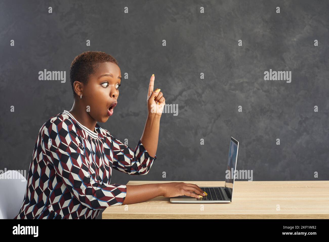Woman sitting at laptop raises index finger up as sign that he came up with bright idea or thought. Stock Photo