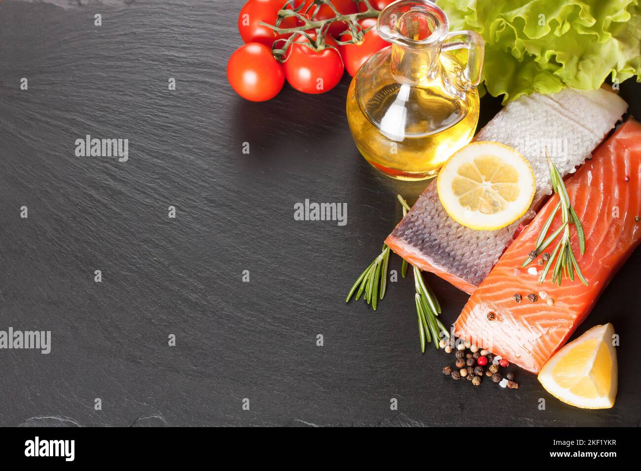 Raw salmon fillet, spices and vegetables on a dark slate background ...