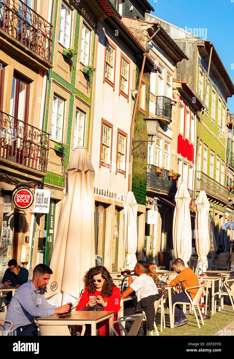 BRAGA, PORTO, PORTUGAL - NOVEMBER 14, 2021: People sitting in street cafe, Santa Cruz church in background, evening sunshine Stock Photo