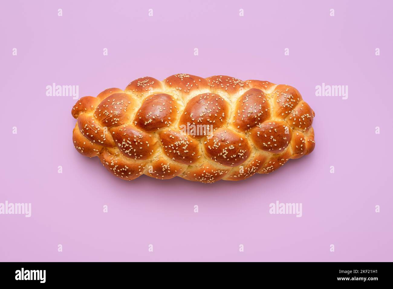 Directly above view with a homemade challah bread minimalist on a purple table. Braided bread, a traditional Jewish recipe, on a vibrant-colored backg Stock Photo