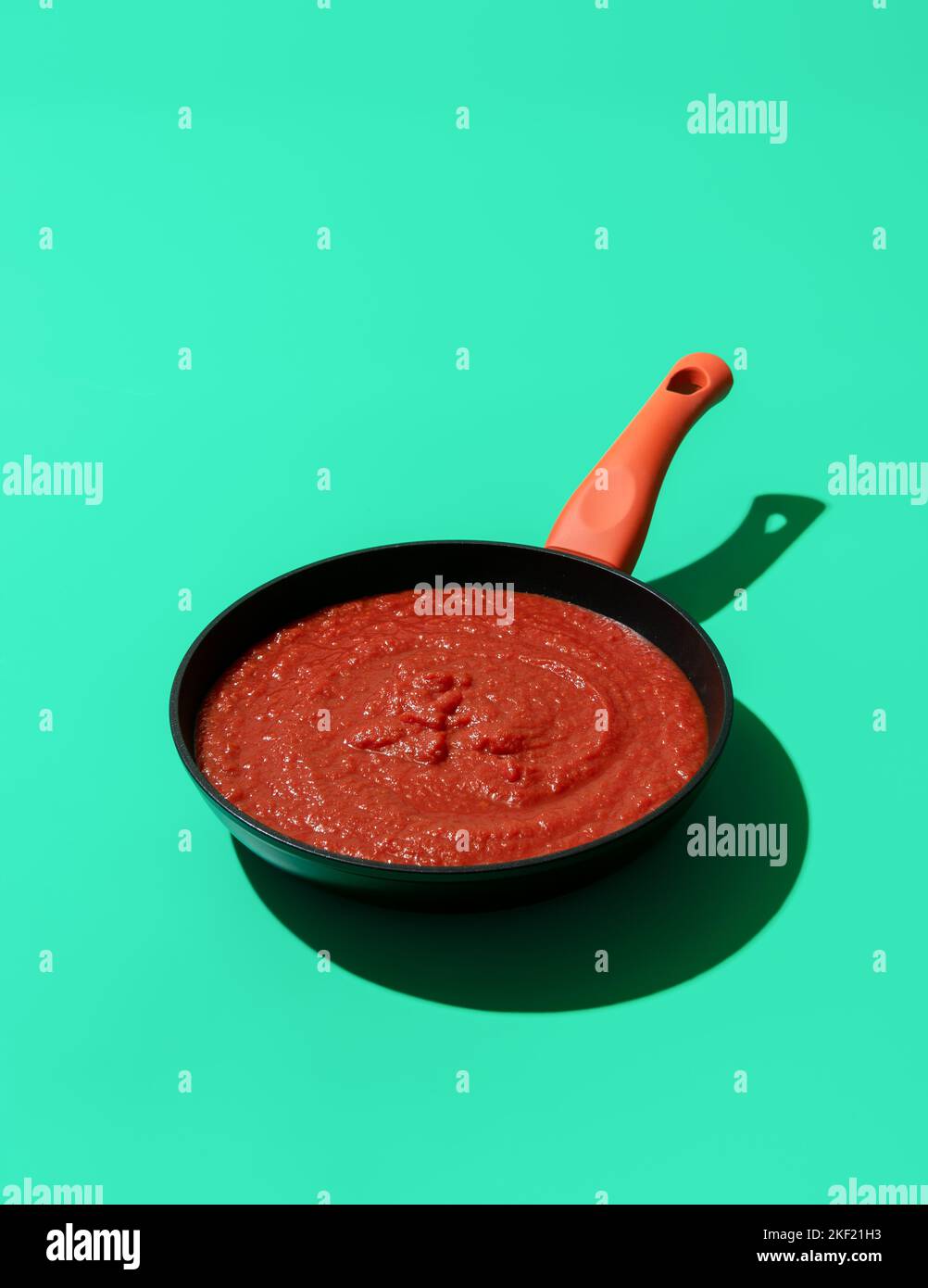 Iron cast pan with tomato sauce minimalist on a green colored table. Traditional italian tomato sauce with basil and garlic, used for pizza or pasta. Stock Photo