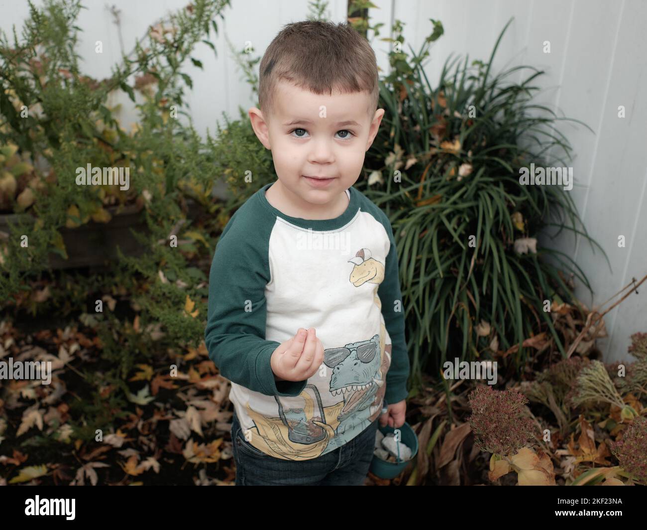 young boy playing in the backyard on a warm day in late autumn, posing among the plants Stock Photo