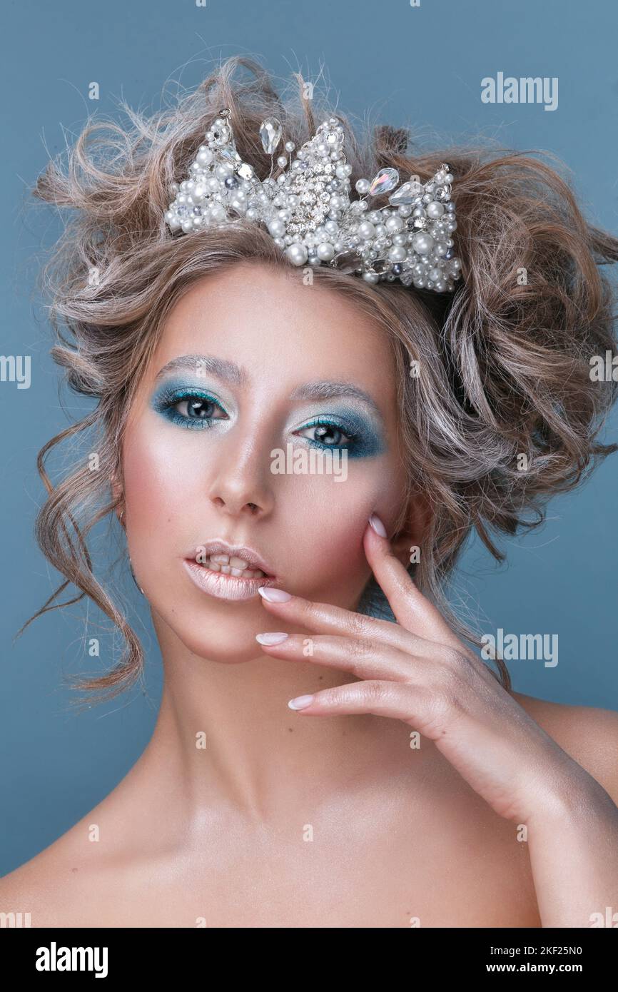 Close-up portrait of winter queen. Beautiful woman with blue eyes in crown on blue studio studio background Stock Photo