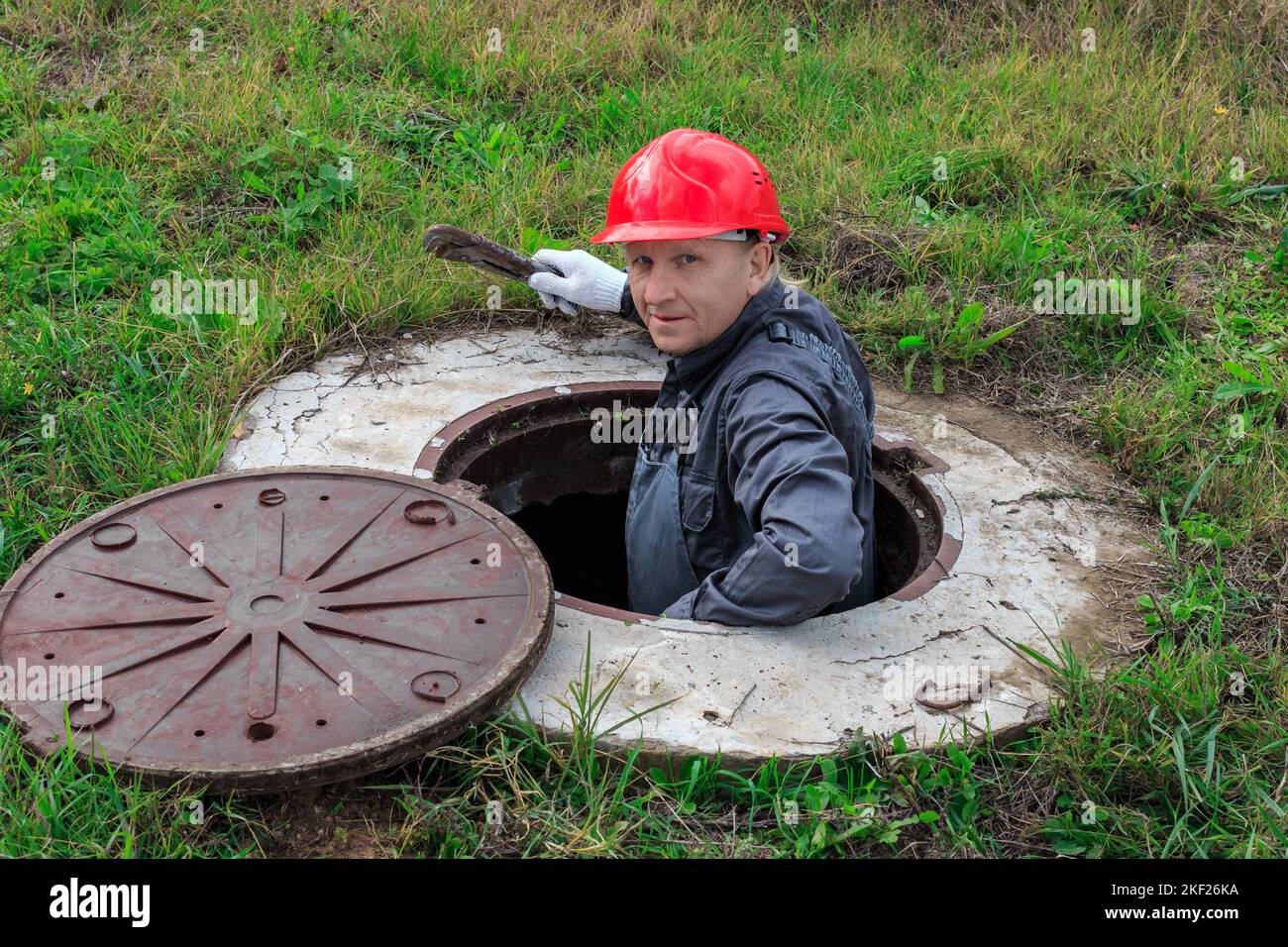 A male plumber in a helmet descended into an open water well for inspection and repair. Stock Photo