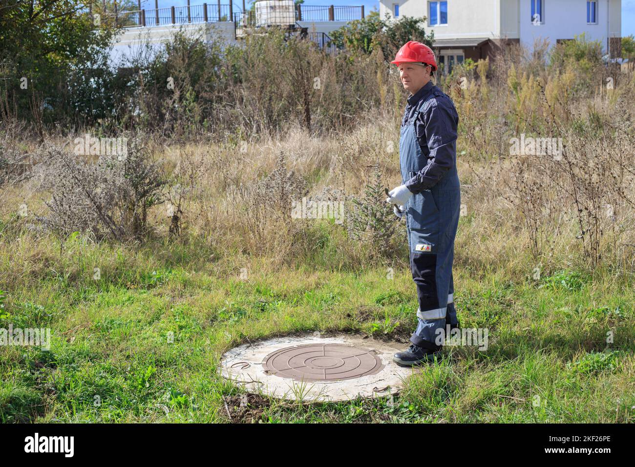 A man in overalls and a hard hat near a water well in the countryside. Inspection of water wells and meters. Stock Photo