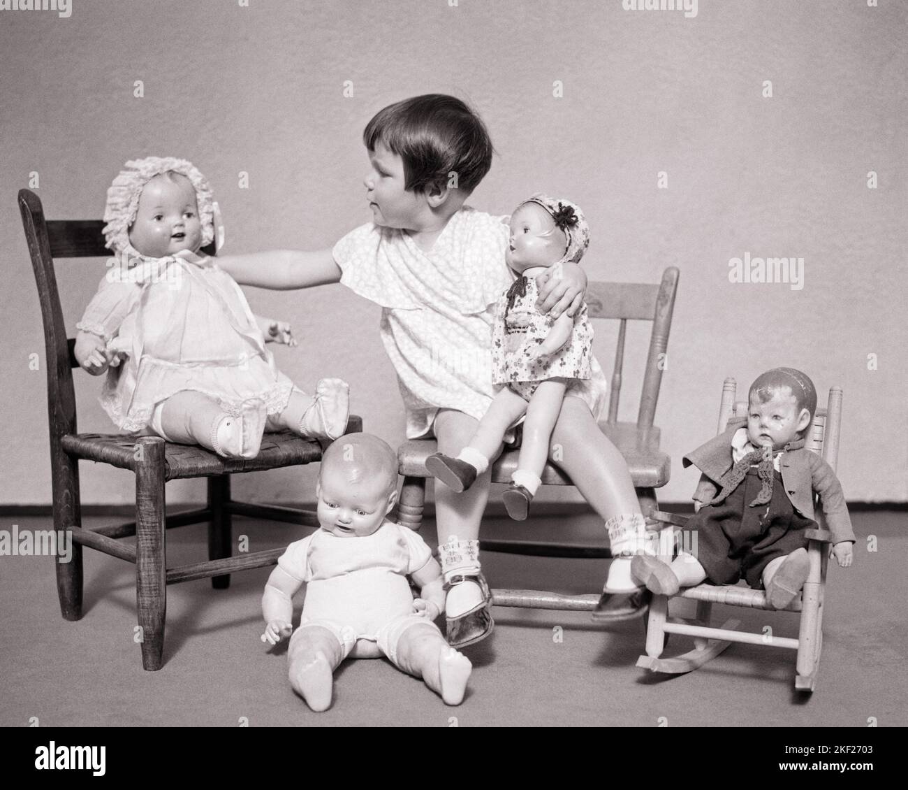 1930s LITTLE BRUNETTE GIRL PLAYING WITH DOLLS GETTING HER VARIOUS DOLLS SEATED IN CHAIRS ON HER LAP OR ON FLOOR BY HER FEET - j4616 HAR001 HARS B&W LAP BRUNETTE GOALS PORCELAIN MODELS CONNECTION STYLISH VARIOUS OR COLLECTIBLES GROWTH JUVENILES TOGETHERNESS BLACK AND WHITE CAUCASIAN ETHNICITY COLLECTIBLE HAR001 OLD FASHIONED Stock Photo