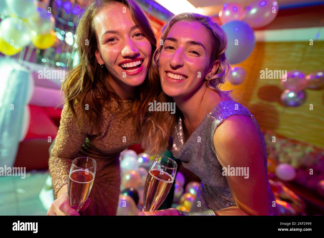 Portrait of two happy caucasian female friends laughing and drinking champagne at a nightclub. Fun, drinking, going out, friendship and party concept. Stock Photo