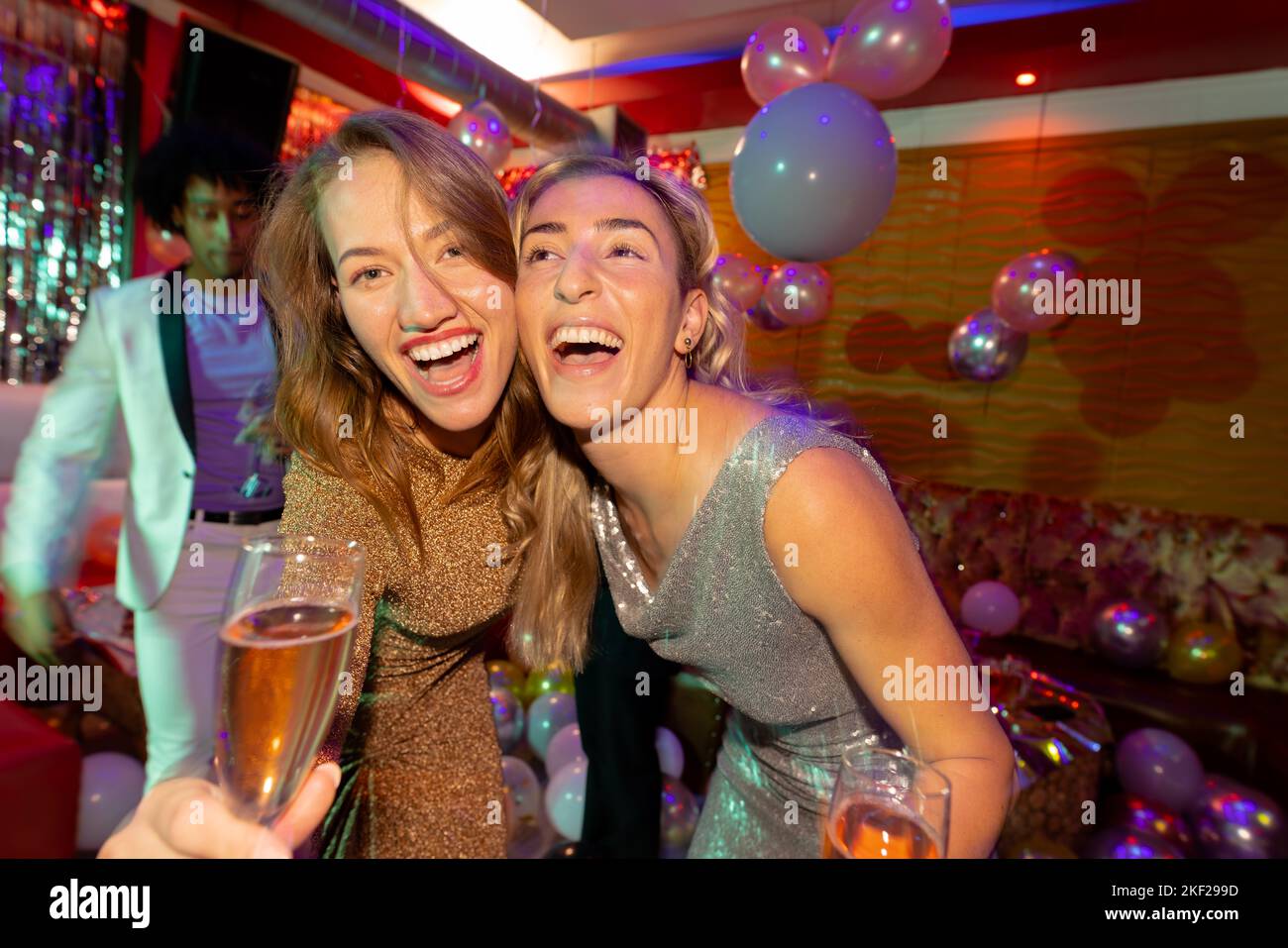 Portrait of two happy caucasian female friends laughing and drinking champagne at a nightclub. Fun, drinking, going out, friendship and party concept. Stock Photo