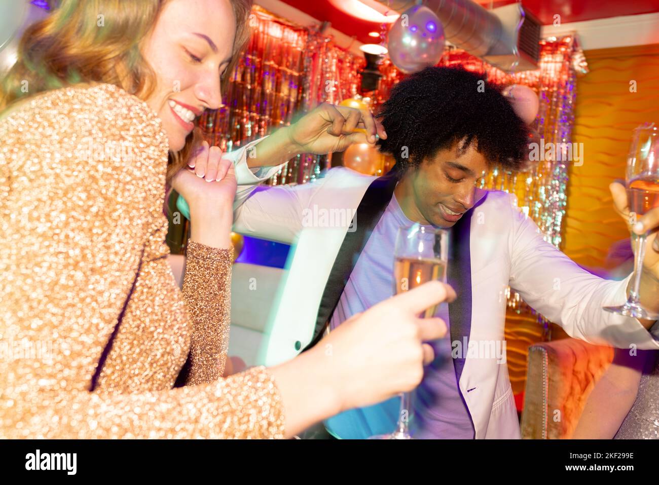 Happy diverse couple dancing and drinking champagne at a nightclub. Fun, drinking, going out, inclusivity and party concept. Stock Photo