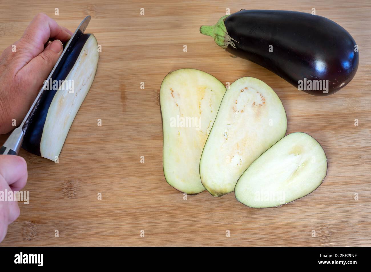 Slicing a Solanum melongena  or  an aubergine on a wooden table Stock Photo