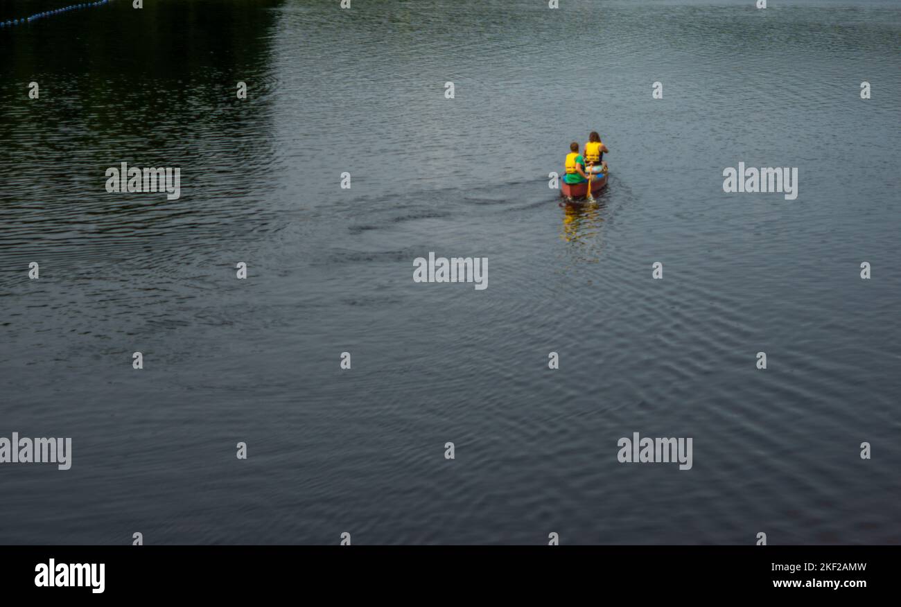 Rear view of a couple in yellow life jacket paddling a canoe on lake