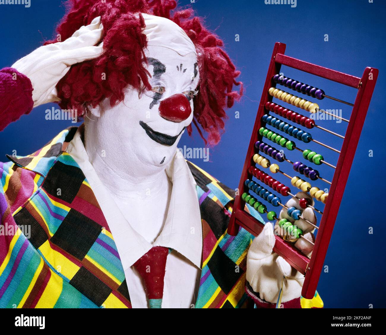 1960s WHITEFACE CLOWN IN RED MOP YARN WIG RED NOSE SCRATCHING HIS HEAD TRYING TO FIGURE NUMBERS ON AN ABACUS COUNTING FRAME - kc2530 HAR001 HARS CLOWNS HUMOROUS HEAD AND SHOULDERS DISCOVERY HIS PERFORMER KNOWLEDGE TRYING MAKE UP COMICAL BEADS ENTERTAINER OCCUPATIONS WHITEFACE CONCEPTUAL CLOWN WHITE COMEDY JESTER SCRATCHING BAFFLED CALCULATIONS MID-ADULT MID-ADULT MAN PRECISION CALCULATING FOOL HAR001 OLD FASHIONED PERPLEXED Stock Photo