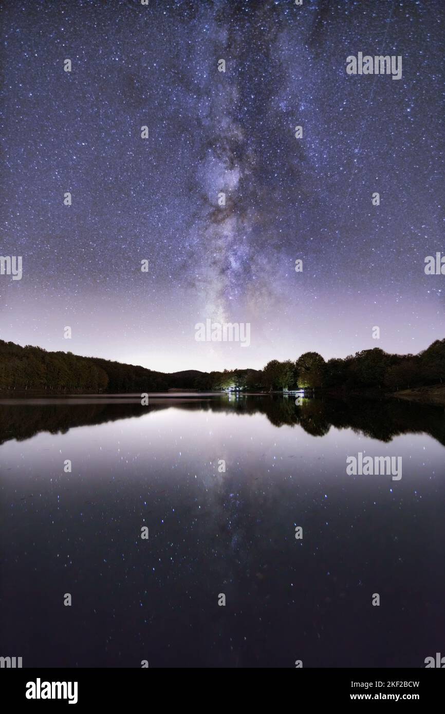 A vertical shot of a starry sky at night, with a cottage on the coast ...