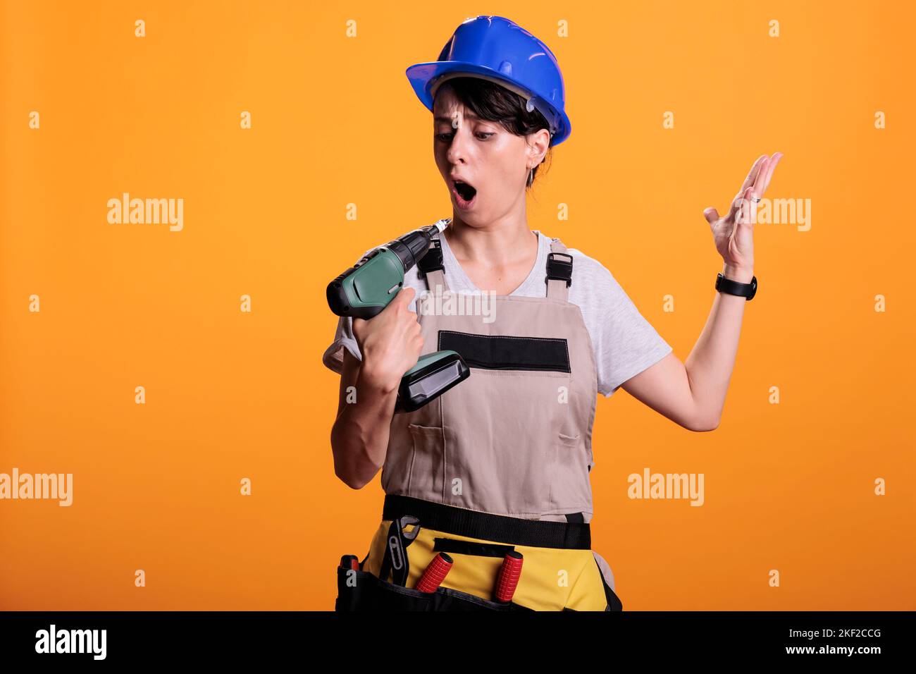 Young cheerful handywoman holding electric nail gun, posing over yellow