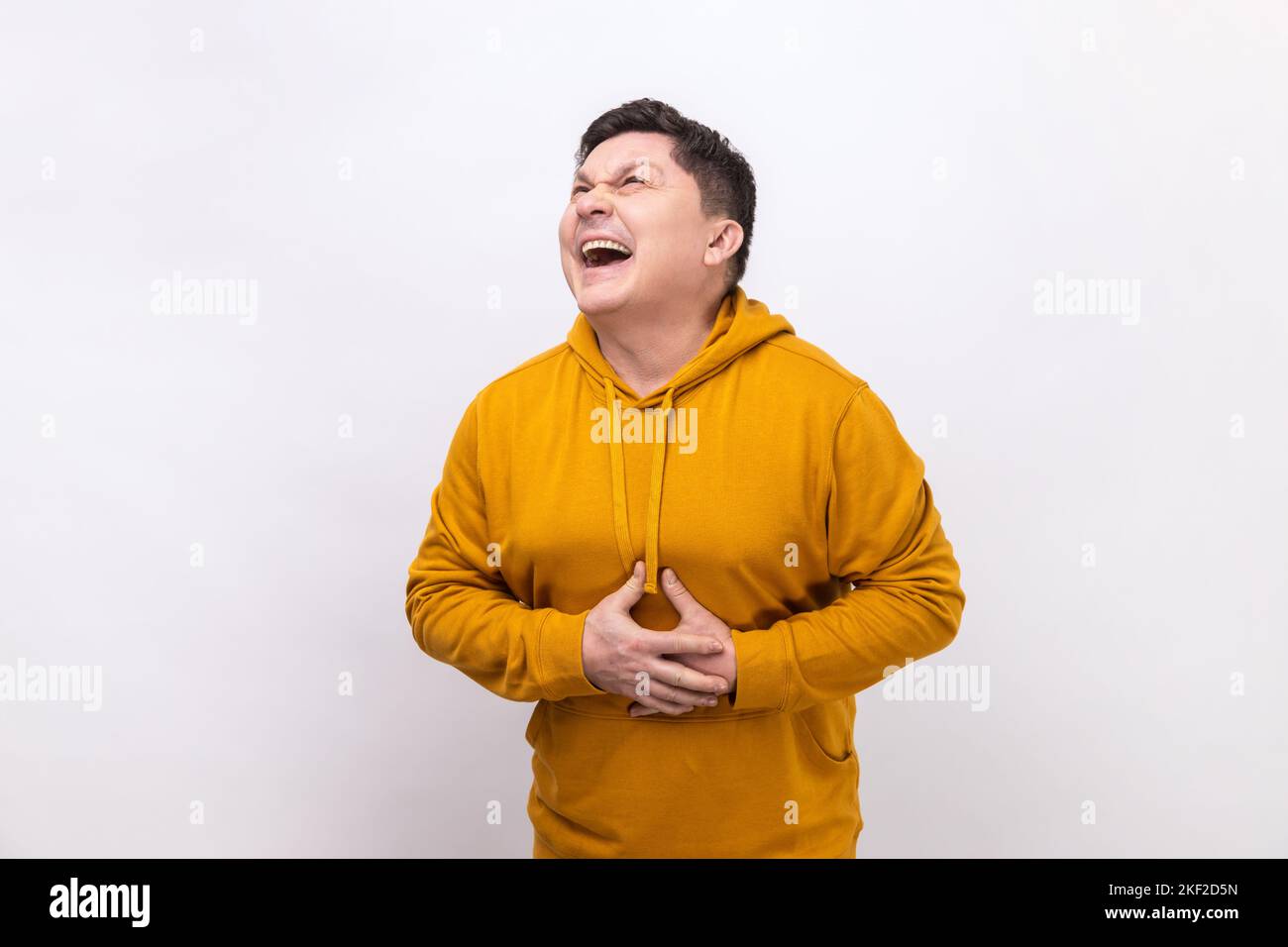 Portrait of extremely excited happy man holding his belly and laughing out loud, chuckling giggling at amusing joke, wearing urban style hoodie. Indoor studio shot isolated on white background. Stock Photo