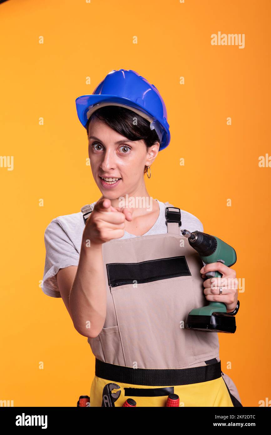 Woman construction worker pointing index finger at camera and holding