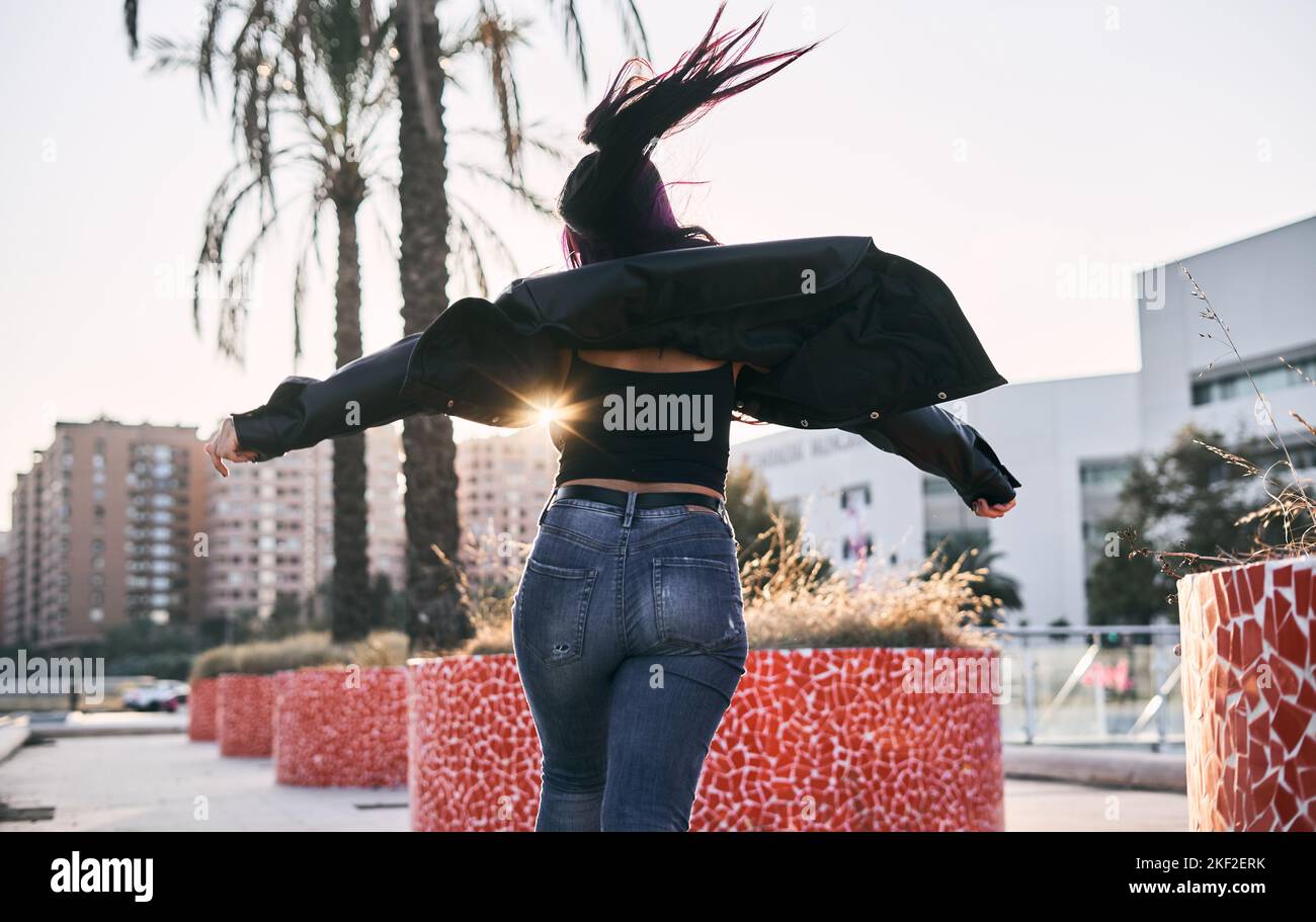 latina girl with brunette fur jacket long hair blue pants dancing with outstretched arms in the city park at sunset Stock Photo