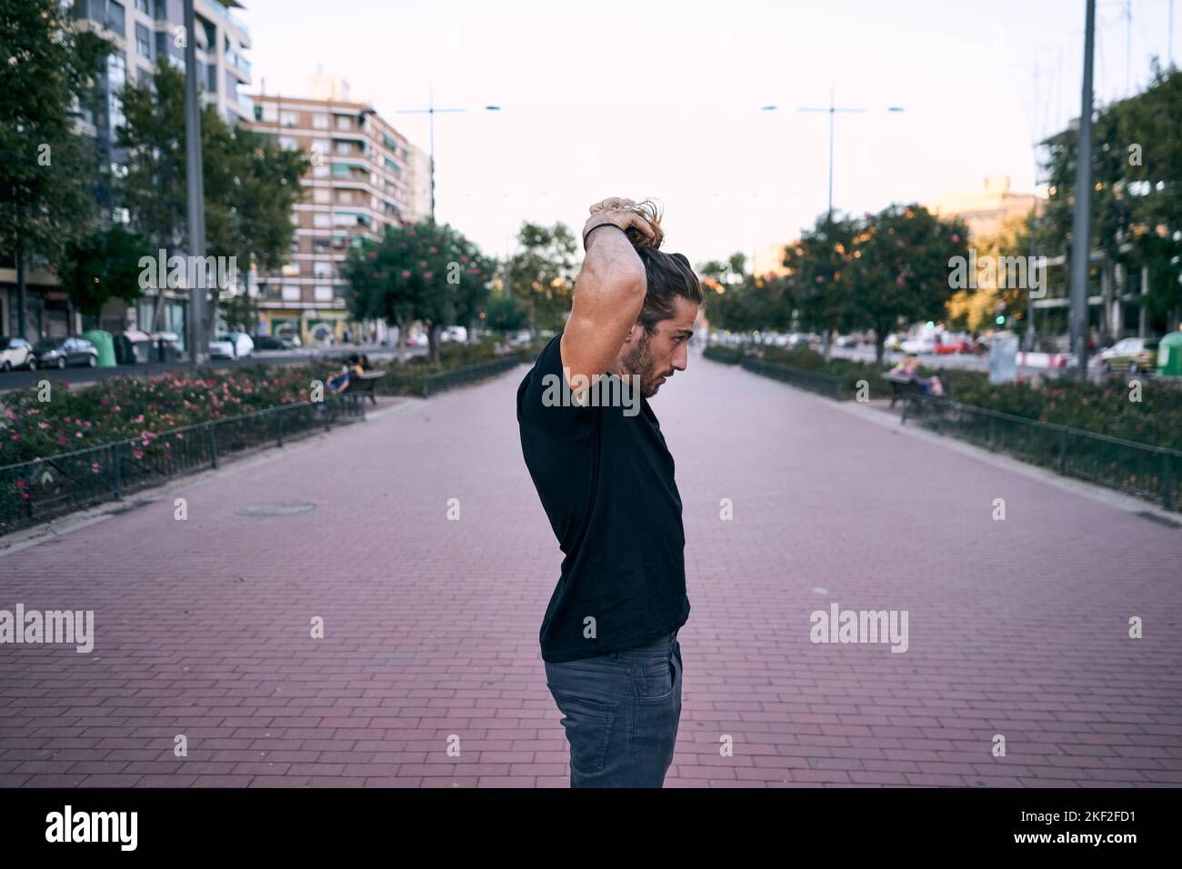 caucasian young man black t-shirt long blond hair making a ponytail in his hair standing on the boulevard in the city Stock Photo