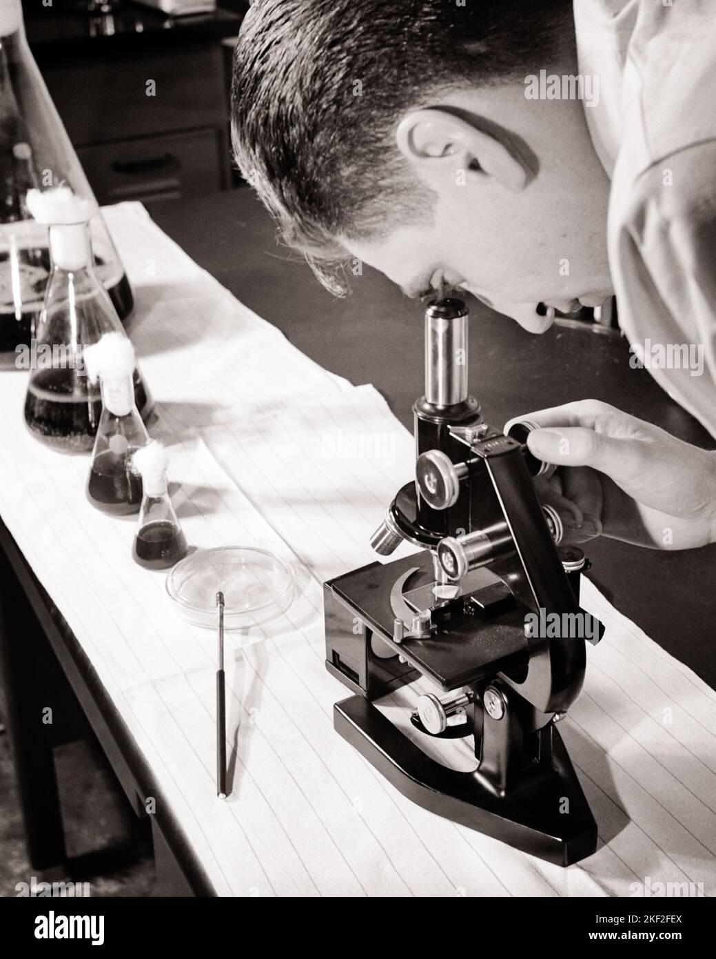 1950s ANONYMOUS MAN SCIENTIST LOOKING AT SLIDE IN MICROSCOPE AND WITH VARIOUS SIZES OF FLASKS WITH MEASURED AMOUNTS OF LIQUID  - l581 HAR001 HARS ADVENTURE DISCOVERY SCIENTIFIC AND PROGRESS INNOVATION MEASURED OCCUPATIONS CONCEPTUAL VARIOUS ANONYMOUS PHARMACOLOGY FLASKS MID-ADULT MID-ADULT MAN SOLUTIONS BLACK AND WHITE CAUCASIAN ETHNICITY HAR001 LABORATORIES LABS OLD FASHIONED SIZES Stock Photo