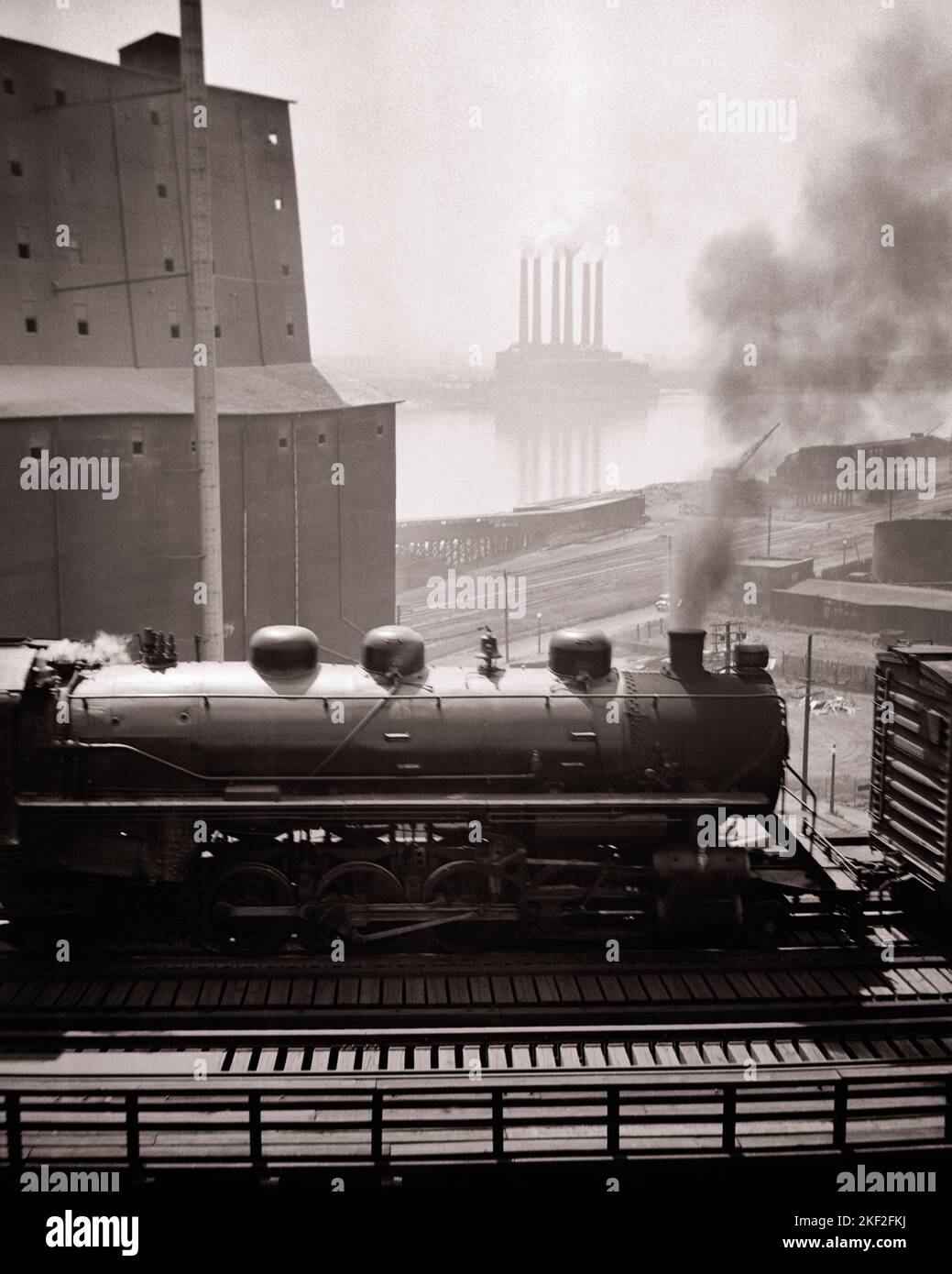 1930s STEAM TRAIN BY GRAIN ELEVATOR MISSISSIPPI RIVER CAHOKIA IL POWER PLANT FROM THE MUNICIPAL BRIDGE ST LOUIS MISSOURI USA - q37738 CPC001 HARS ELEVATOR CONCEPT CONCEPTUAL INFRASTRUCTURE RAILROADS SYMBOLIC CONCEPTS GROWTH BLACK AND WHITE CLOUDY IL MIDWEST MIDWESTERN MISSISSIPPI MO MUNICIPAL OLD FASHIONED REPRESENTATION SMOKY ST LOUIS Stock Photo