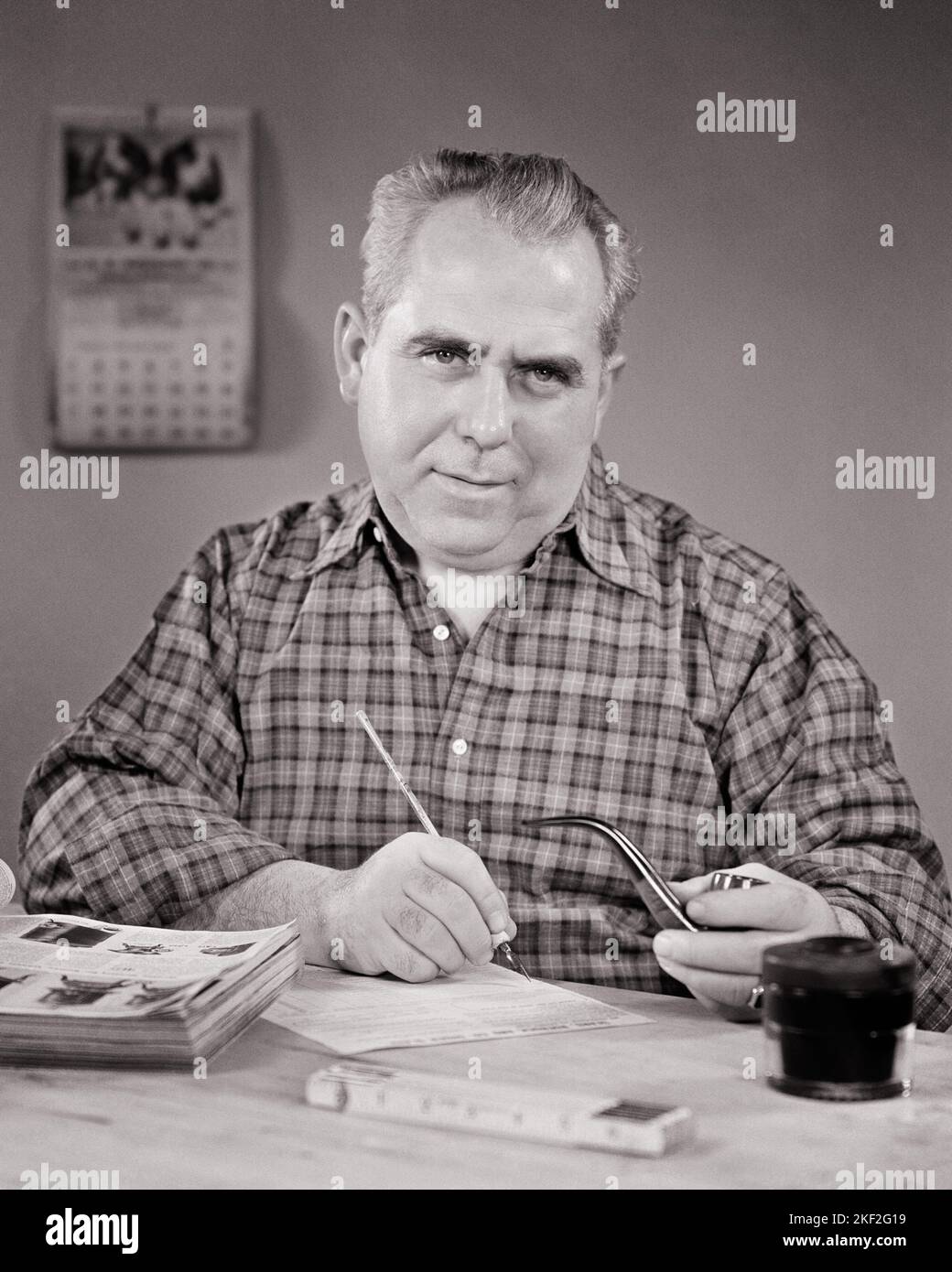 1940s MATURE MAN SITTING AT DESK WRITING AN ORDER FROM AN OPEN CATALOG WITH STEEL TIP PEN HOLDING A PIPE LOOKING AT CAMERA - s11119 HAR001 HARS MALES PLANNING ORDER EXPRESSIONS MIDDLE-AGED B&W MIDDLE-AGED MAN EYE CONTACT PIPES TOBACCO CHOICE HOPEFUL BAD HABIT OCCUPATIONS SMOKER NICOTINE ADDICTIVE TIP CATALOG PURCHASING ORDERING RELAXATION BLACK AND WHITE CAUCASIAN ETHNICITY HAR001 OLD FASHIONED Stock Photo