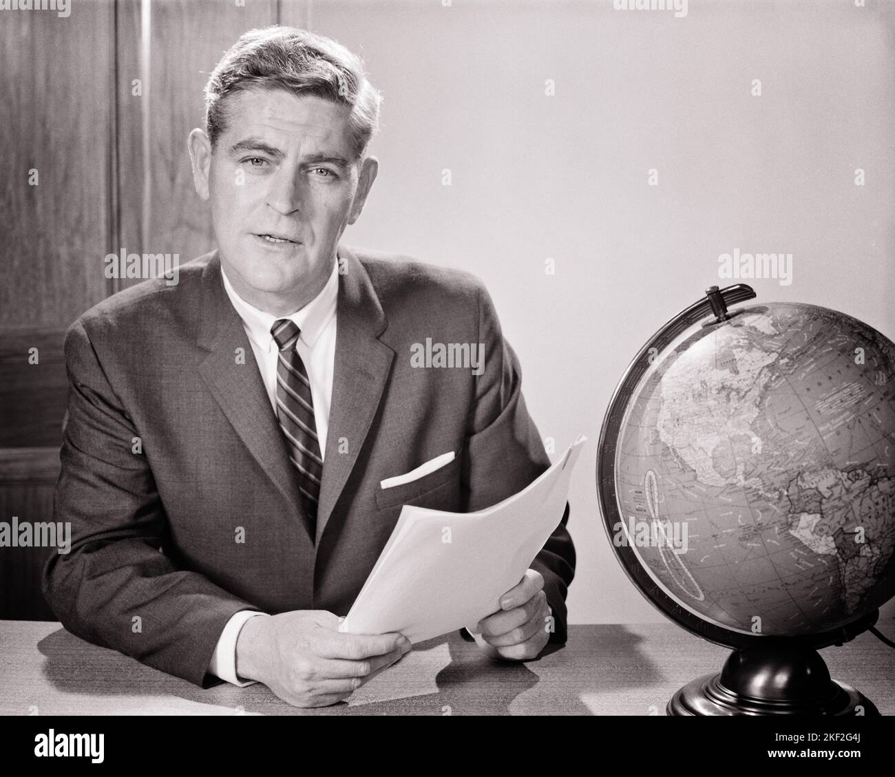 1960s MAN READING FROM DOCUMENT SEATED AT DESK WITH WORLD GLOBE LOOKING AT CAMERA TEACHER NEWSMAN ANNOUNCER BROADCASTER SPEAKER - s11506 HAR001 HARS JOURNALIST B&W EYE CONTACT TELEVISIONS BROADCASTER SUIT AND TIE RADIOS BROADCASTING DOCUMENT GLOBAL ANNOUNCER AUDIO INSTRUCTOR AUTHORITY OCCUPATIONS EDUCATOR CHANNELS EDUCATING EDUCATORS INSTRUCTORS MID-ADULT MID-ADULT MAN NEWSMAN SCHOOL TEACHES WORLDWIDE BLACK AND WHITE CAUCASIAN ETHNICITY HAR001 INTERCONTINENTAL INTERNATIONAL OLD FASHIONED Stock Photo