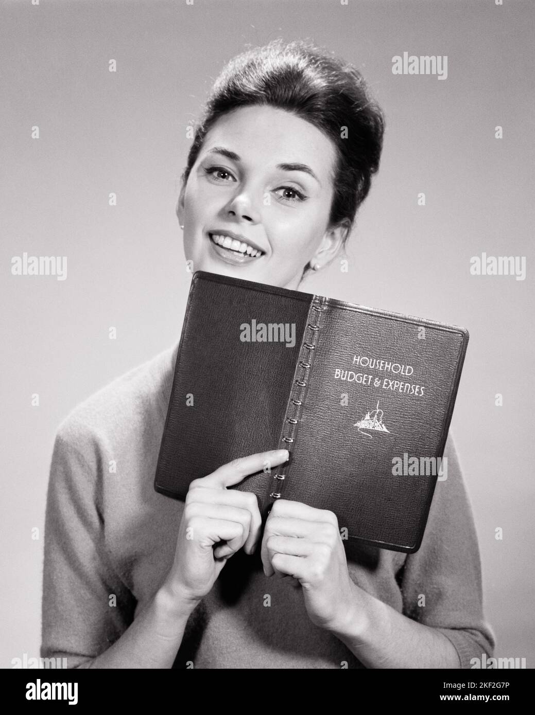 1950s smiling brunette housewife holding ledger of household budget