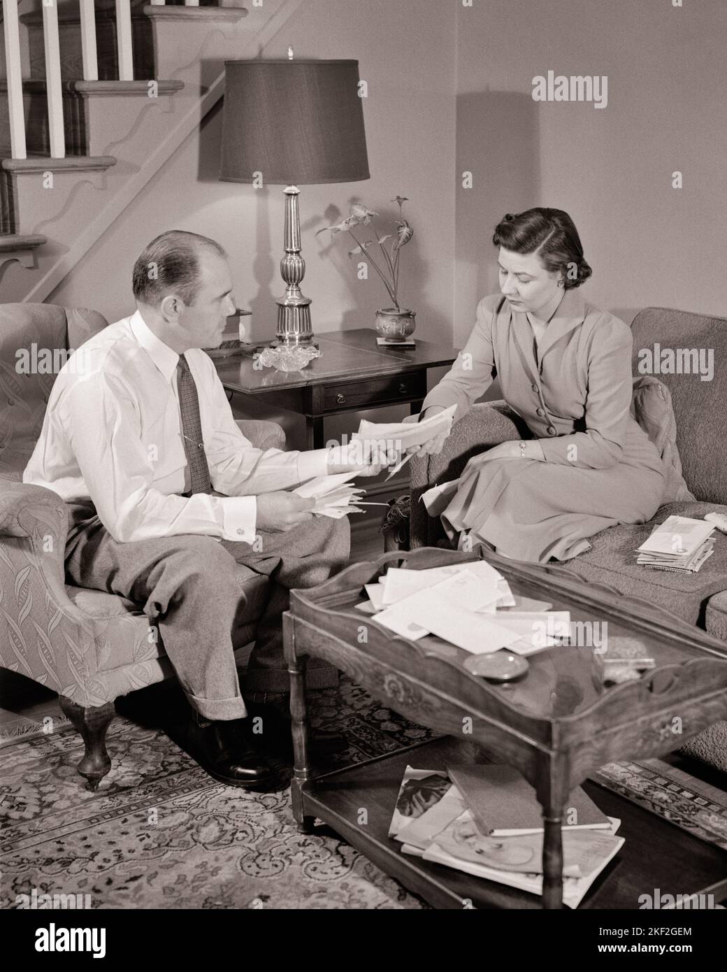 1950s MAN AND WOMAN HUSBAND AND WIFE SITTING AROUND THE COFFEE TABLE REVIEWING DISCUSSING HOUSEHOLD BUDGET BILLS AND EXPENSES - s2116 HAR001 HARS LIFESTYLE FEMALES MARRIED STUDIO SHOT SPOUSE HUSBANDS HOME LIFE FINANCES COPY SPACE FULL-LENGTH LADIES PERSONS MALES B&W PARTNER GOALS HIGH ANGLE DISCUSSING LIVING ROOM AND TO CONNECTION REVIEWING SHIRT AND TIE COOPERATION EXPENSES MID-ADULT MID-ADULT MAN MID-ADULT WOMAN TOGETHERNESS WIVES BLACK AND WHITE CAUCASIAN ETHNICITY COFFEE TABLE HAR001 OLD FASHIONED Stock Photo