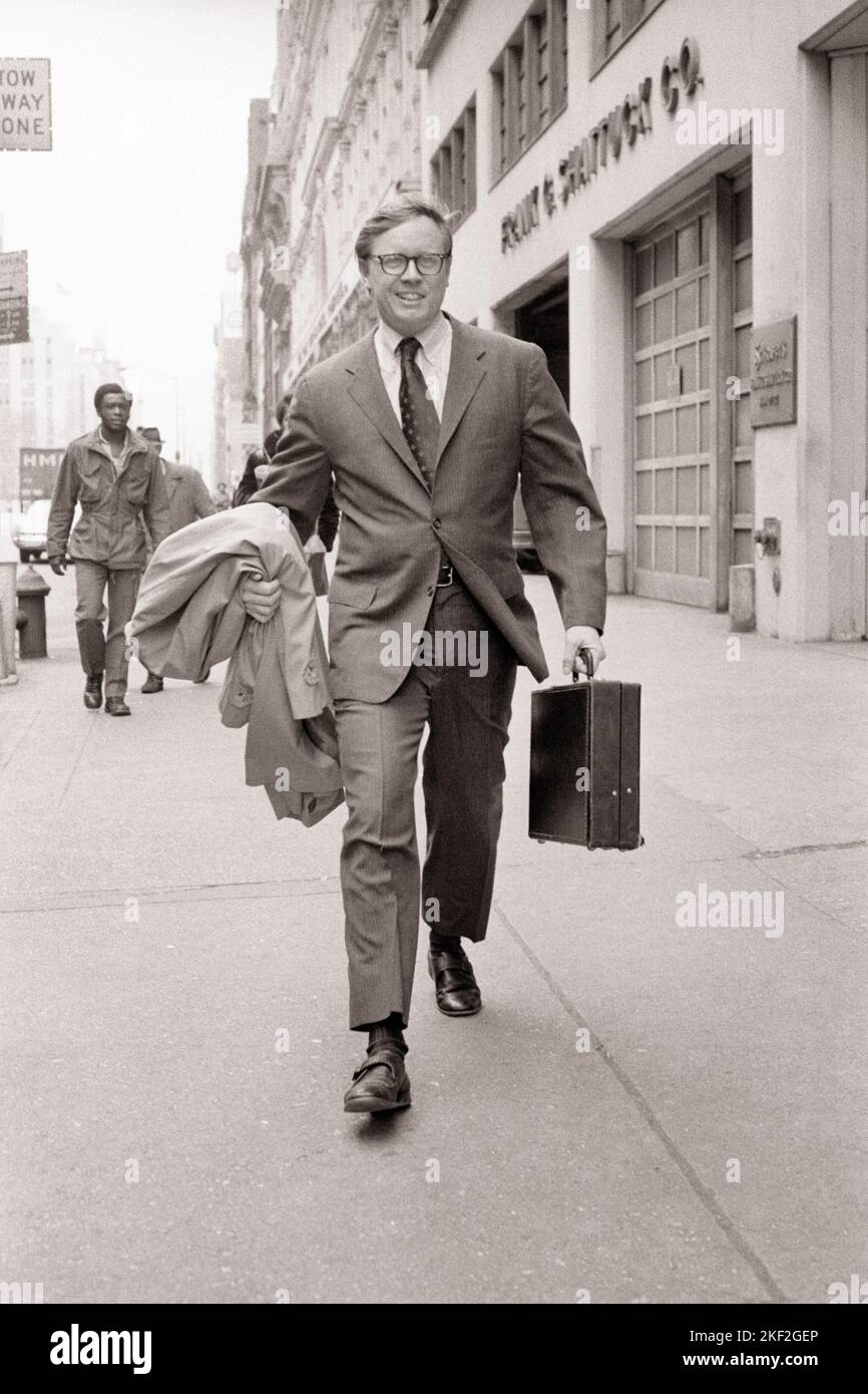 1970s SALESMAN WALKING ON CITY STREET CARRYING RAIN COAT ON ARM AND