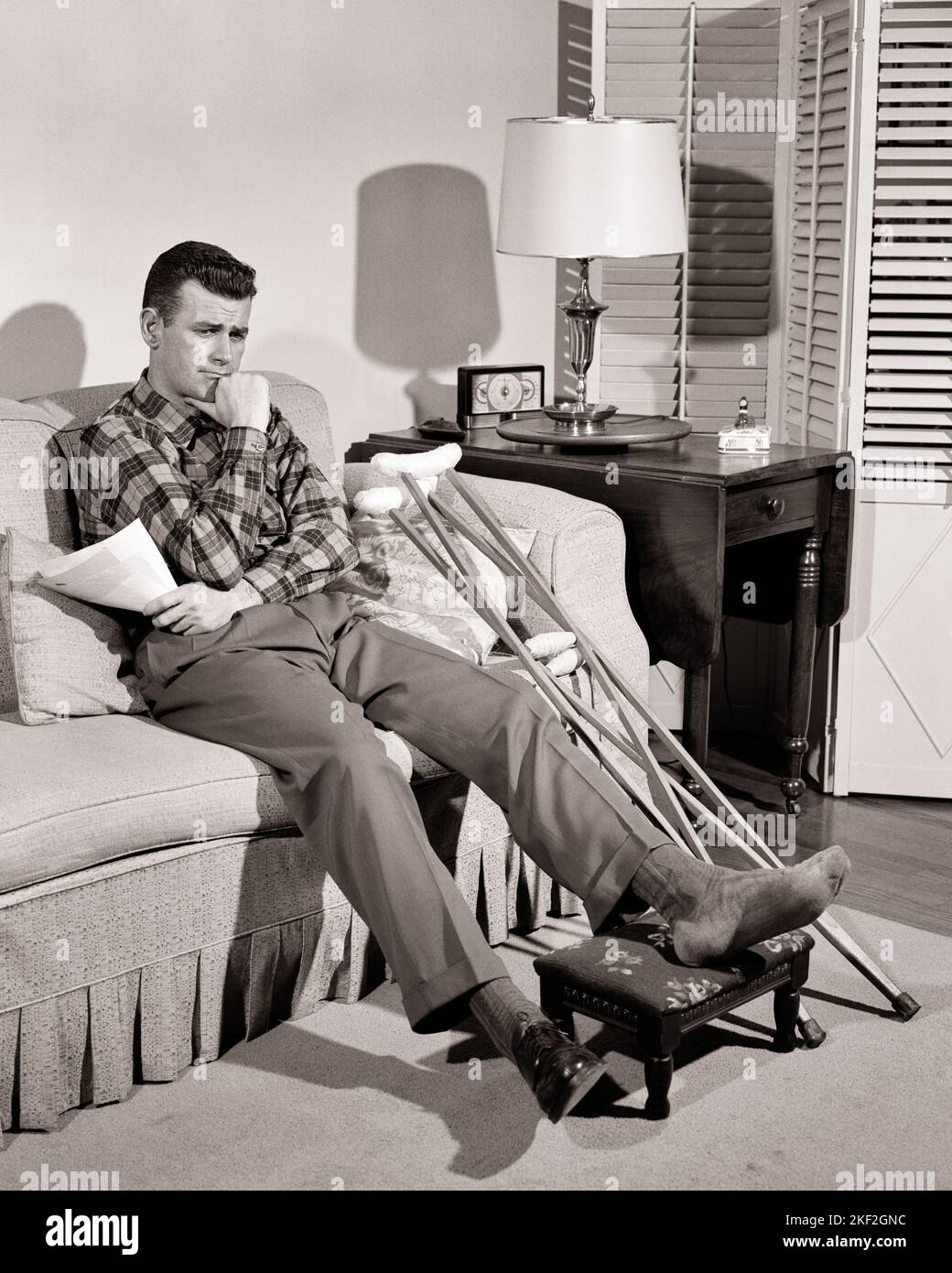 1950s WORRIED MAN HOLDING HANDFUL OF BILLS WHILE SITTING ON LIVING ROOM SOFA WITH CRUTCHES AND HIS INJURED FOOT UP ON A STOOL - s4373 HAR001 HARS ILLNESS HOME LIFE COPY SPACE FULL-LENGTH PERSONS MALES RISK TROUBLED B&W CONCERNED SADNESS HEALTHCARE DISASTER PREVENTION HIGH ANGLE HIS HEALING STRATEGY ACCIDENTAL AND DIAGNOSIS PRIDE HEALTH CARE UP IMPAIRMENT MOOD TREATMENT ACCIDENTS GLUM MISHAP CATASTROPHE HANDFUL MID-ADULT MID-ADULT MAN MISERABLE MISFORTUNE SOLUTIONS YOUNG ADULT MAN BLACK AND WHITE CAUCASIAN ETHNICITY DISEASE HAR001 INVOICES OLD FASHIONED Stock Photo