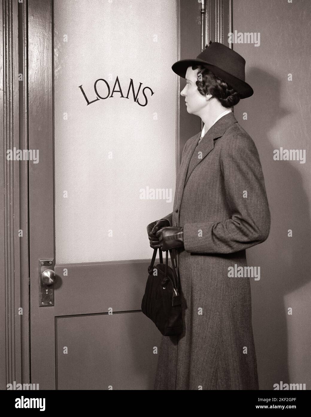 1930s WOMAN STANDING IN FRONT OF DOOR TO LOAN LOANS OFFICE WEARING HAT COAT GLOVES AND CLUTCHING HER HANDBAG - s4410 HAR001 HARS ANGER FEAR DEBT WORRY LIFESTYLE FEMALES PROUD STUDIO SHOT MOODY FINANCES COPY SPACE HALF-LENGTH LADIES PERSONS BANKING BANKER TROUBLED B&W CONCERNED FINANCIAL SADNESS LOAN STYLES AND PRIDE HARDSHIP MOOD CONCEPTUAL GLUM EMBARRASSMENT STYLISH SUPPORT IN FRONT OF FASHIONS IDEAS MID-ADULT MID-ADULT WOMAN MISERABLE NEED SOLUTIONS BLACK AND WHITE CAUCASIAN ETHNICITY CLUTCHING HAR001 LOANS OLD FASHIONED Stock Photo