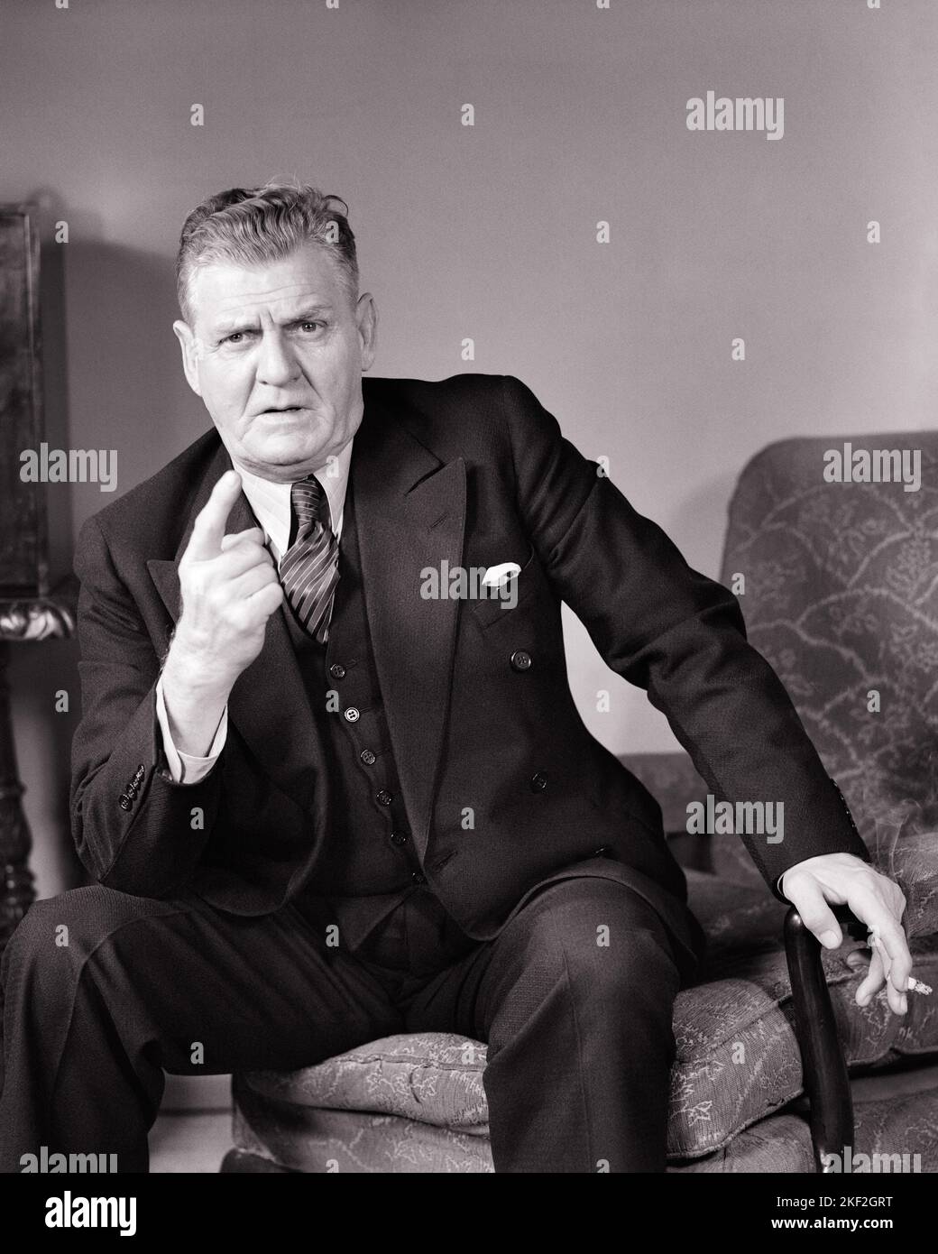 1940s ANGRY MAN POINTING INDEX FINGER SMOKING A CIGARETTE WEARING A FASHIONABLE THREE PIECE SUIT LOOKING STERNLY AT THE CAMERA - s6013 HAR001 HARS ANNOYED STUDIO SHOT HOME LIFE LUXURY MANAGER COPY SPACE HALF-LENGTH PERSONS MALES EXECUTIVES GESTURING VEST BANKER MIDDLE-AGED B&W MIDDLE-AGED MAN EYE CONTACT CIGARETTES INDEX SUIT AND TIE DISTRESSED TOBACCO IRATE EXCITEMENT LEADERSHIP POLITICIAN POWERFUL PRIDE AUTHORITY BAD HABIT GESTURES OCCUPATIONS POLITICS SMOKER NICOTINE BOSSES THREE PIECE SUIT ADDICTIVE STYLISH DISPLEASURE HOSTILITY ANNOYANCE EMOTION EMOTIONAL IRRITATED MANAGERS Stock Photo