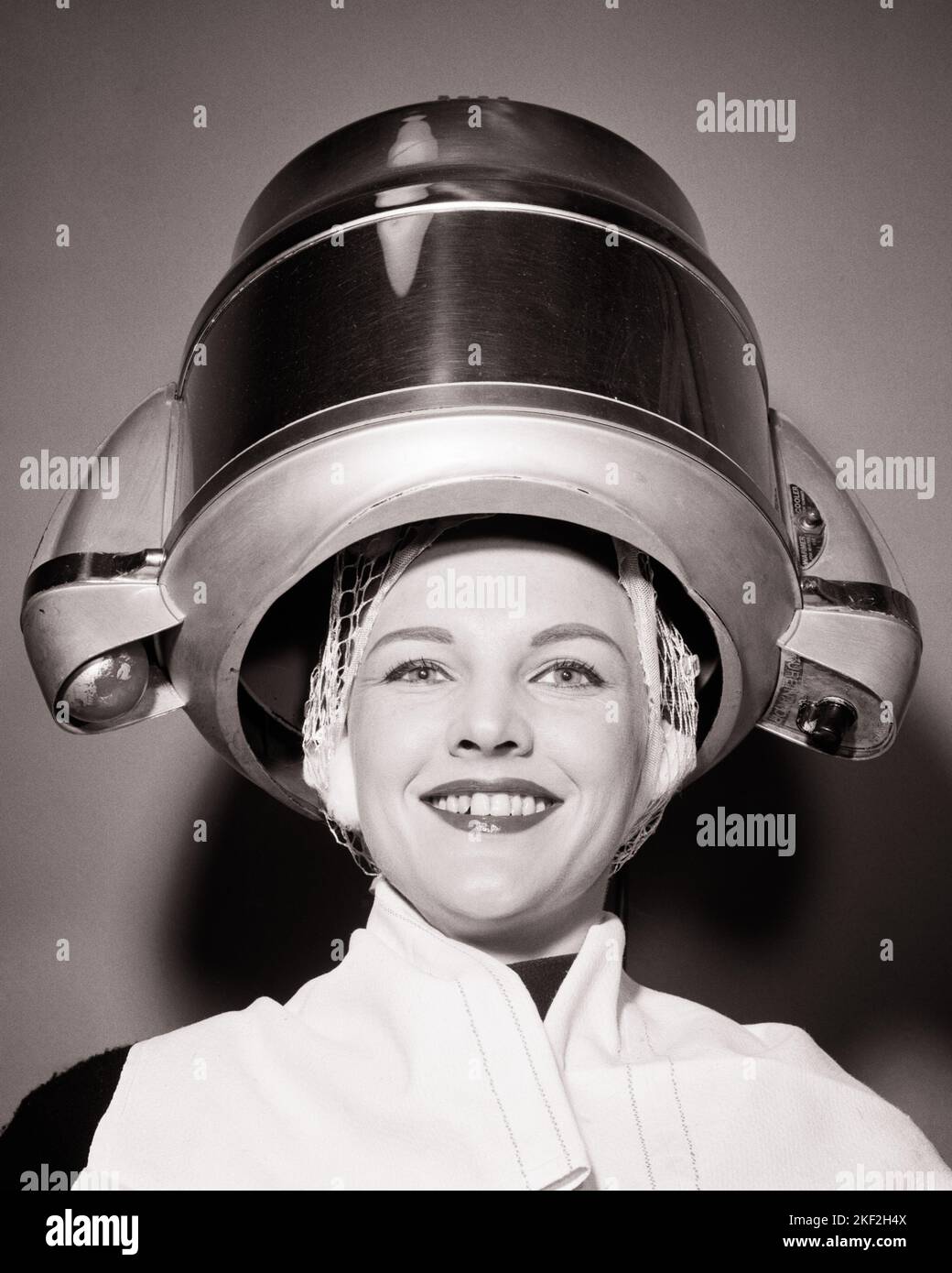 1950s WOMAN UNDER SALON HAIR DRYER WITH TOWEL ON SHOULDERS AND HAIR NET LOOKING AT CAMERA SMILING - s8931 DEB001 HARS HOOD PLEASED JOY LIFESTYLE SATISFACTION FEMALES STUDIO SHOT HEAT COPY SPACE LADIES PERSONS EXPRESSIONS B&W EYE CONTACT HUMOROUS HAPPINESS HEAD AND SHOULDERS CHEERFUL DRYING HAIRDRYER AND EXCITEMENT HAIRSTYLE MACHINES COMICAL SMILES DRYERS BEAUTY PARLOR COMEDY JOYFUL STYLISH DEB001 HAIR NET HAIRDO YOUNG ADULT WOMAN BLACK AND WHITE CAUCASIAN ETHNICITY OLD FASHIONED Stock Photo