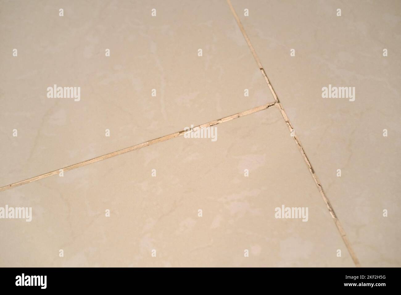 Crack in grouting between white marble tiles. Decaying floor. Bathroom